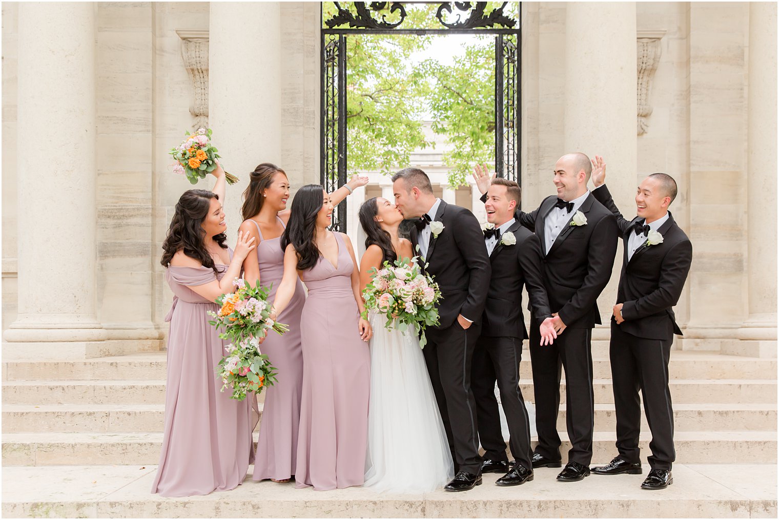 bride and groom kiss with wedding party cheering on the steps at the Rodin Museum
