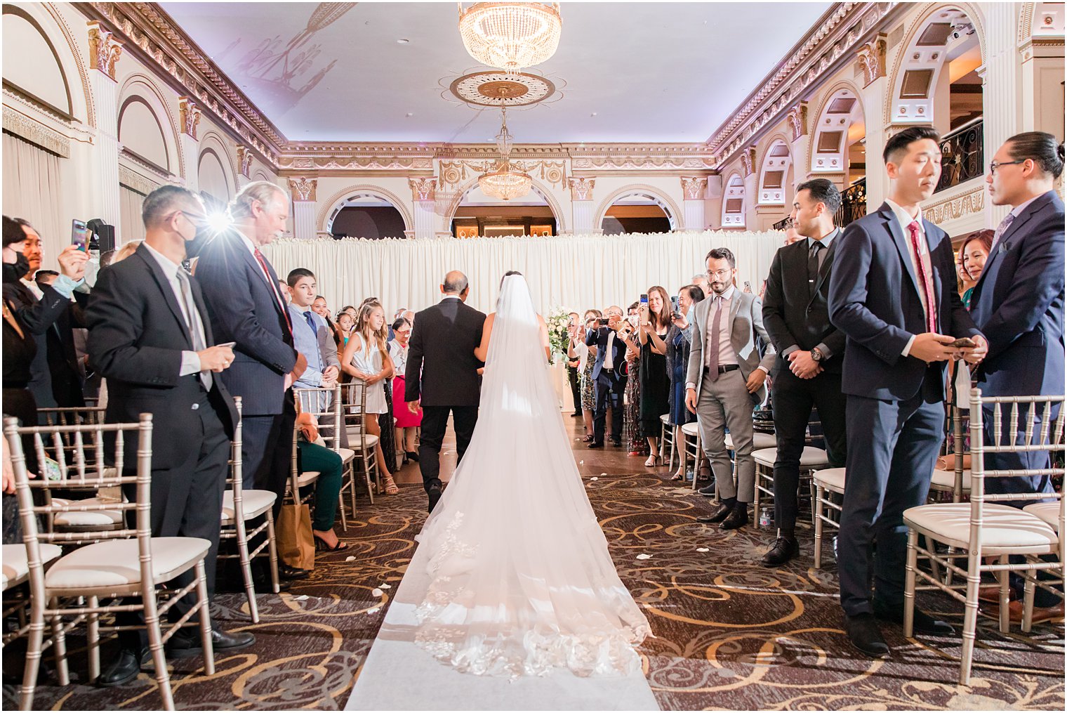 bride walks down aisle with veil behind her during ceremony at the Ballroom at the Ben