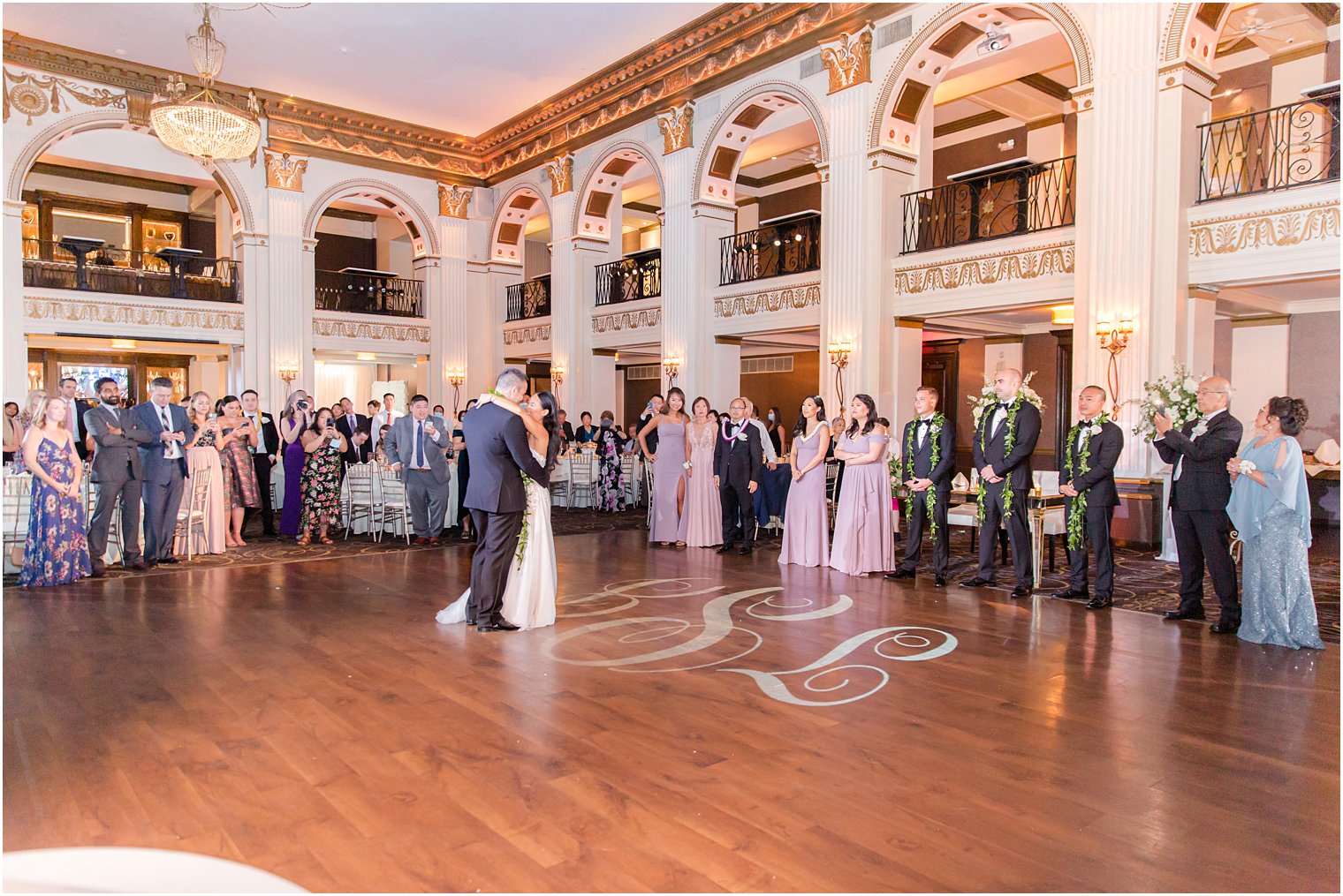 newlyweds have first dance on ballroom dance floor with monogram in lights