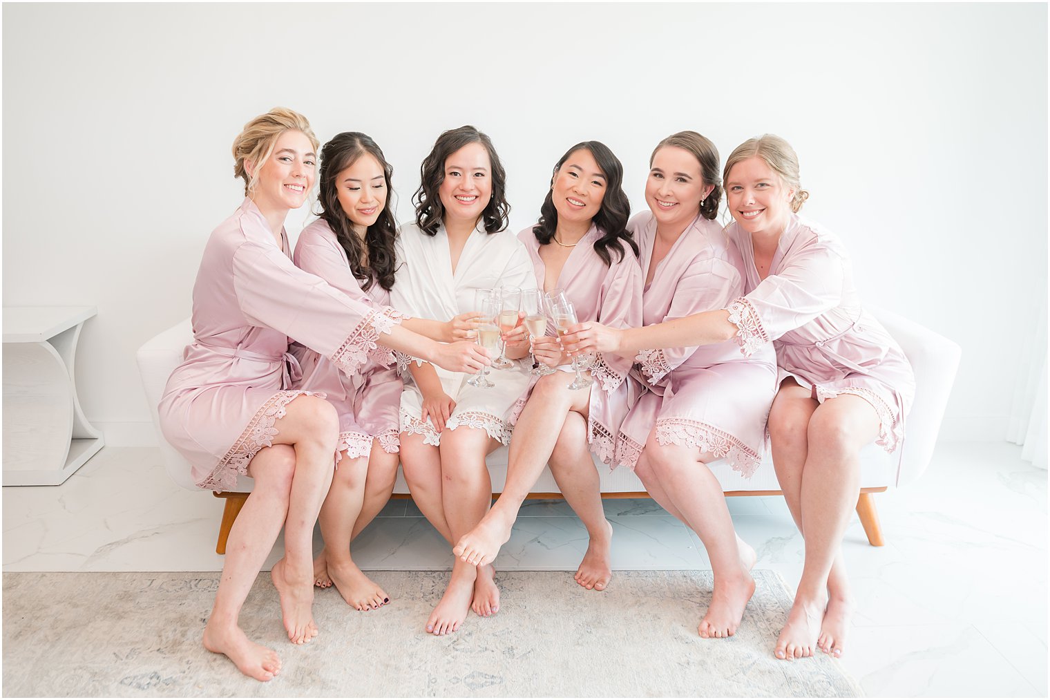 bride sits with bridesmaids in pink robes before beach wedding