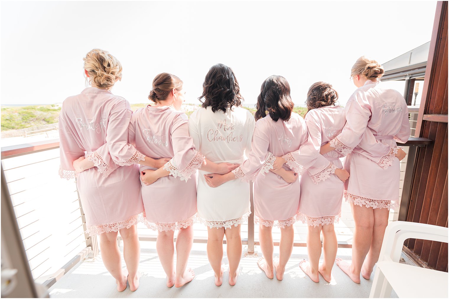 bride poses on deck with bridesmaids in matching pink robes