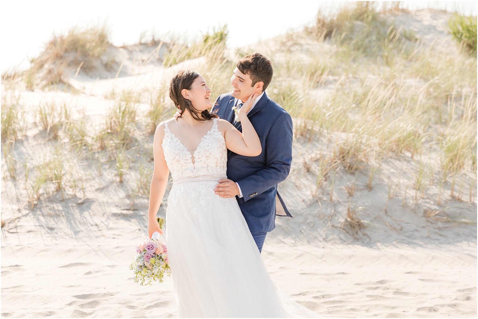 bride looks over shoulder at groom standing on beach