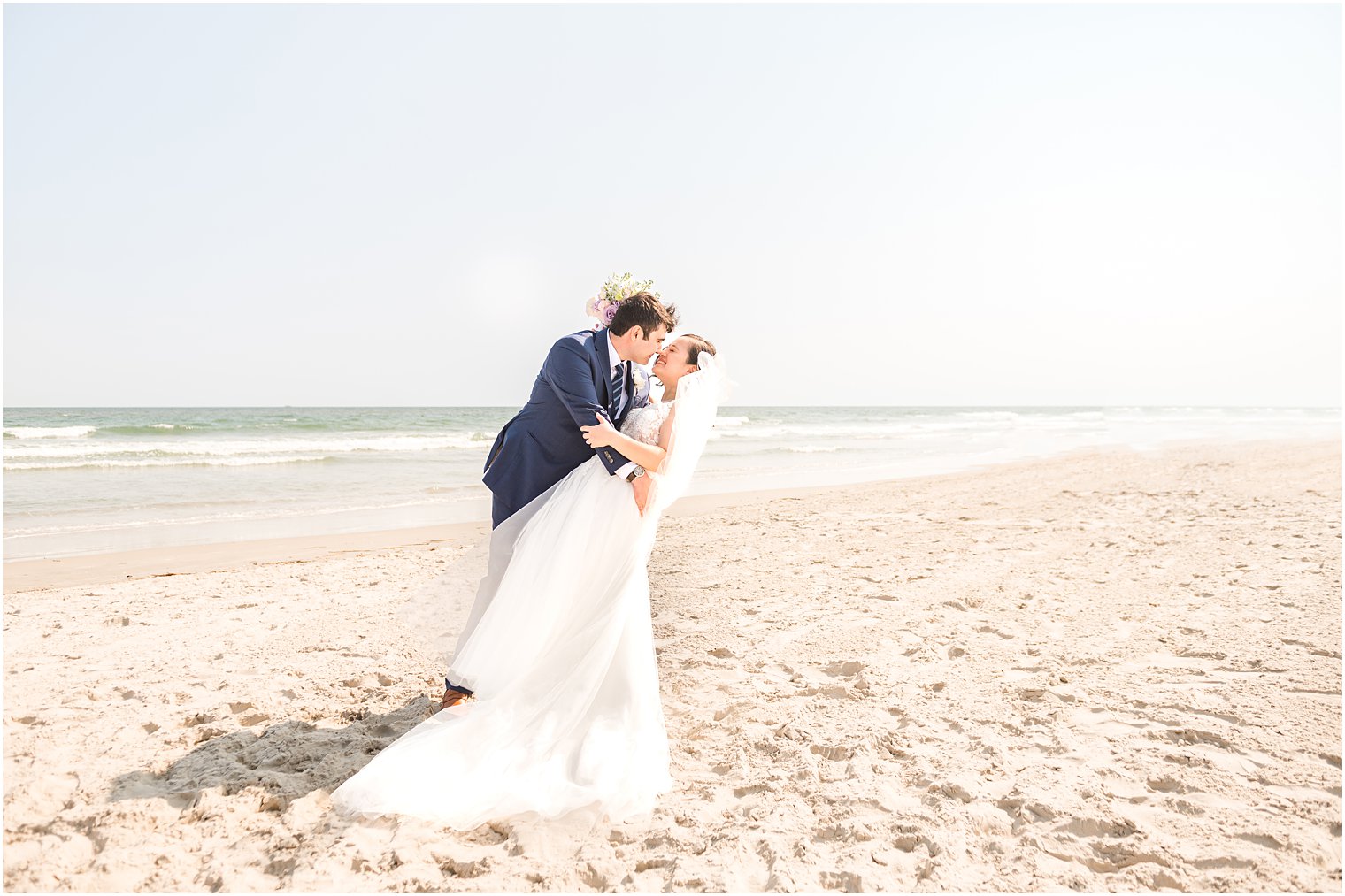 groom kiss bride dipping her standing on sand at Avalon NJ beach 