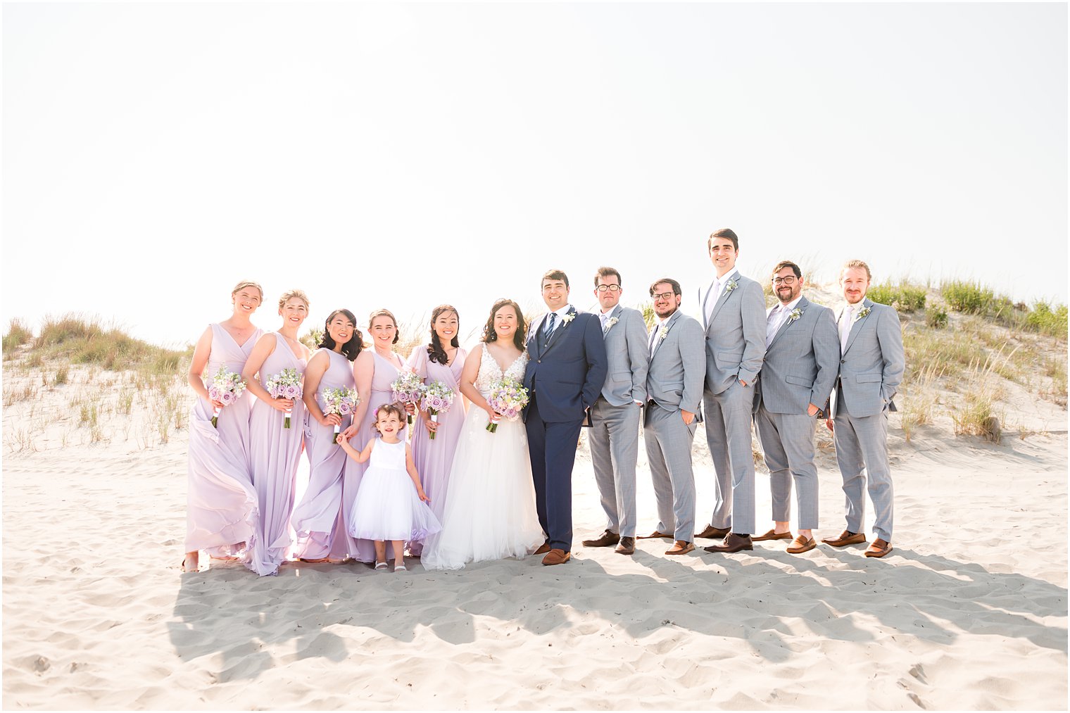 newlyweds stand with wedding party in light purple dresses and grey suits 