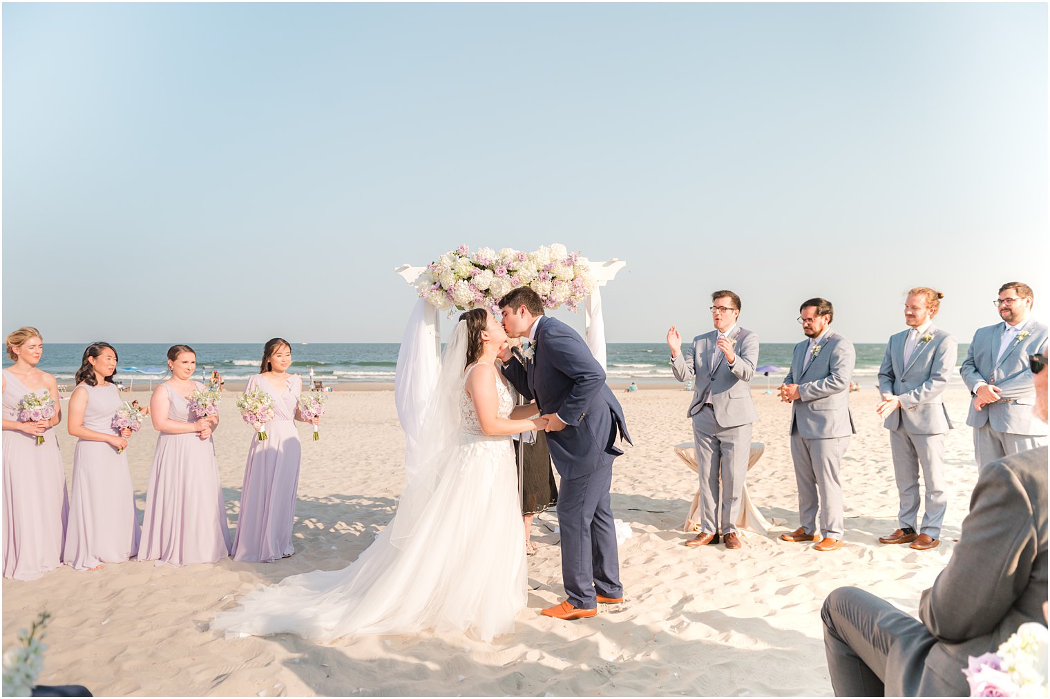 bride and groom kiss by white arbor during beach wedding ceremony in Avalon NJ