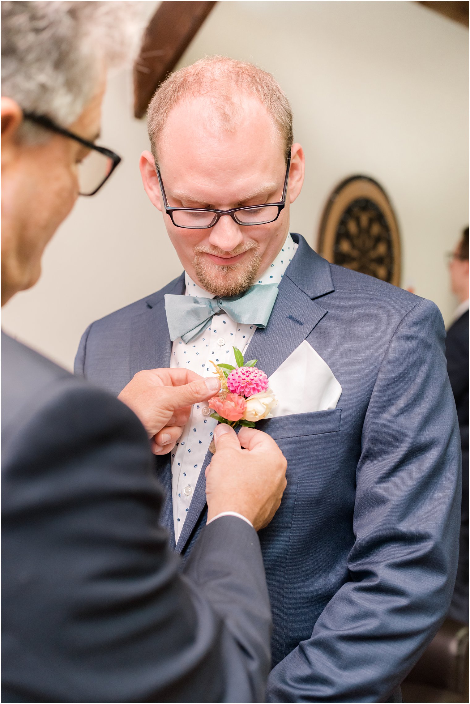father helps groom with pink boutonniere of wildflowers 