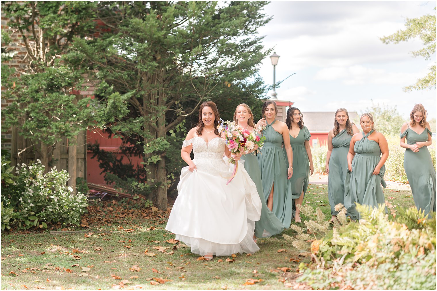 bride walks with bridesmaids to first look in field at Bishop Hall Farmstead