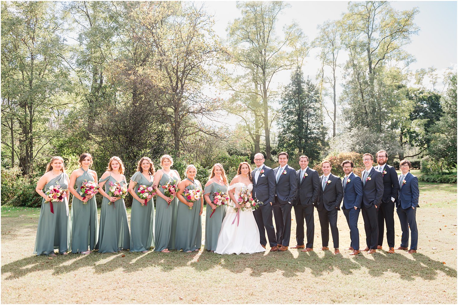 newlyweds stand with wedding party in sea glass green gowns and navy suits 