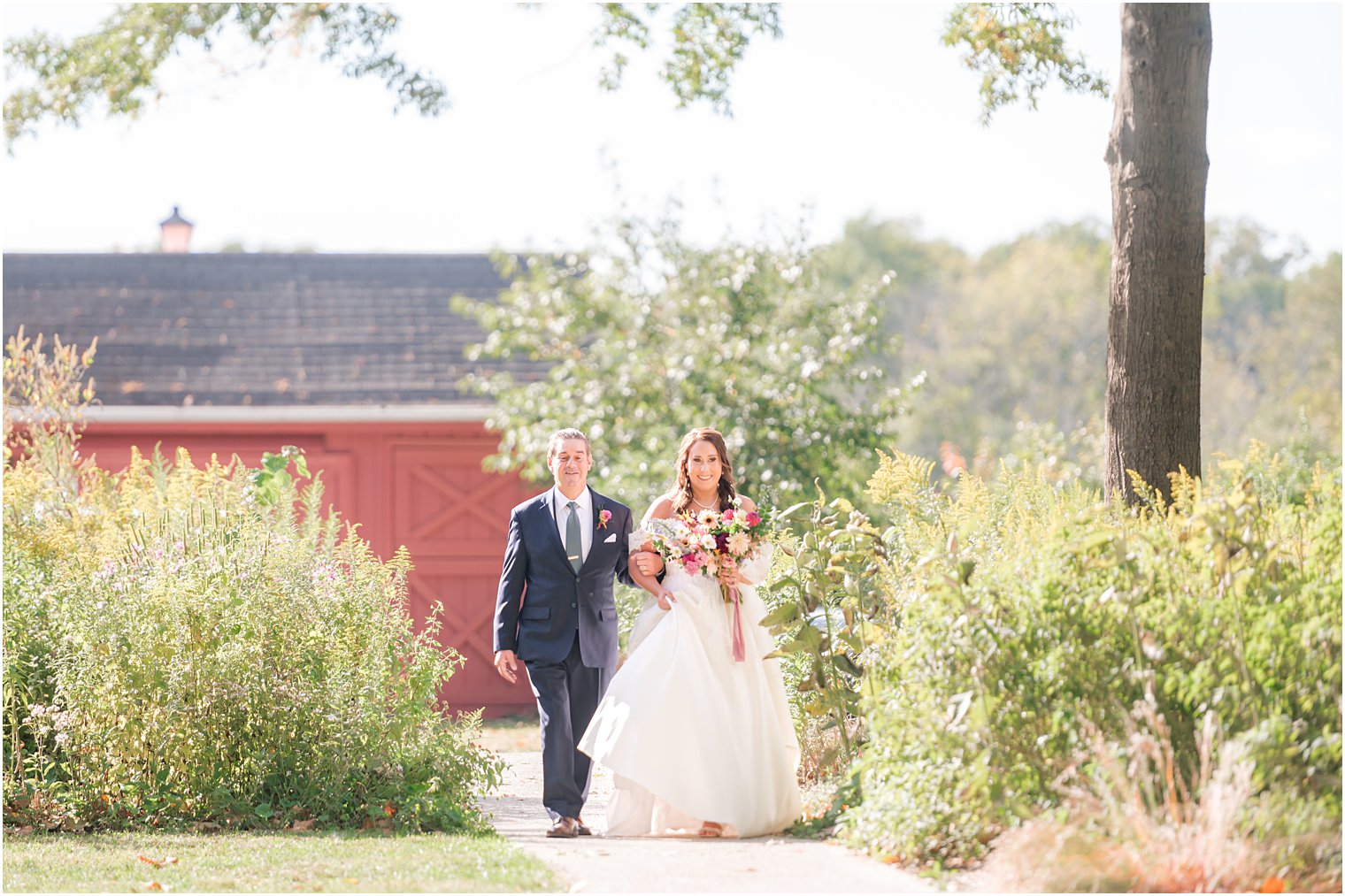 bride walks with father into fall wedding ceremony outdoors on lawn at Bishop Hall Farmstead