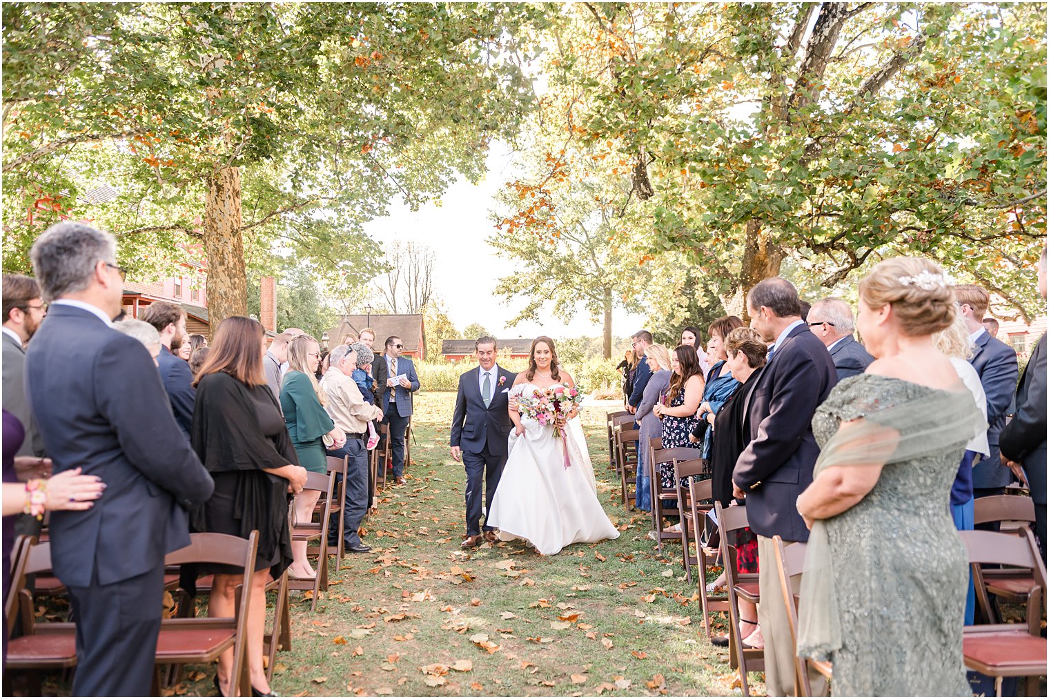 bride walks with dad up aisle at fall wedding ceremony outdoors on lawn at Bishop Hall Farmstead
