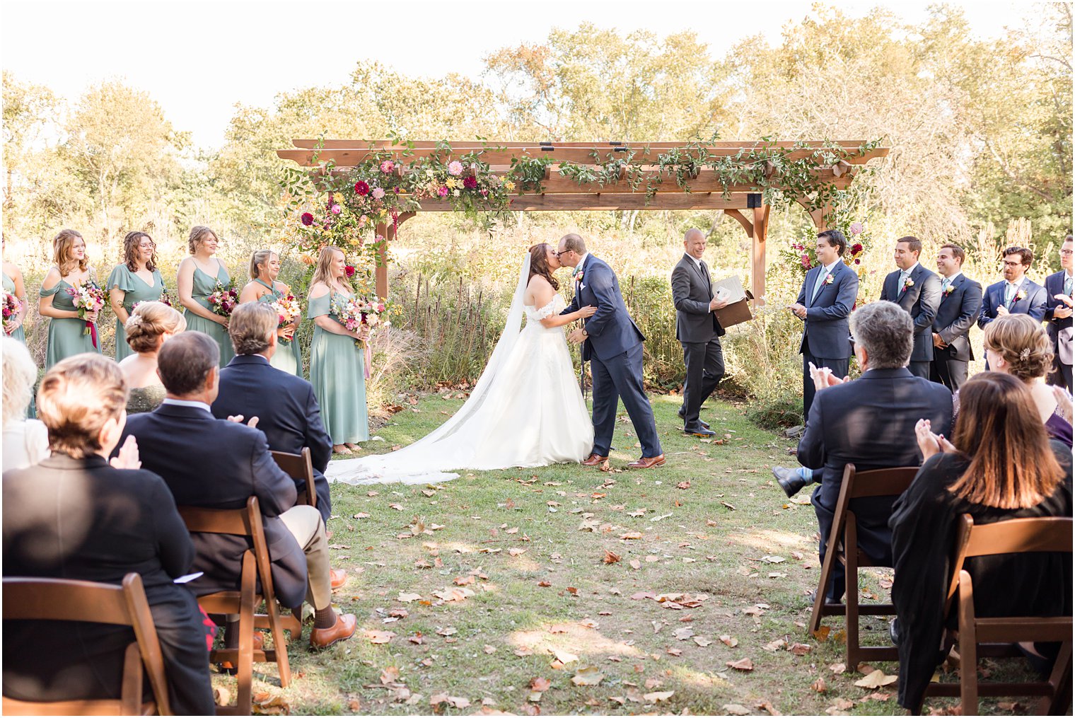 newlyweds kiss under wooden arbor during fall wedding ceremony outdoors on lawn at Bishop Hall Farmstead