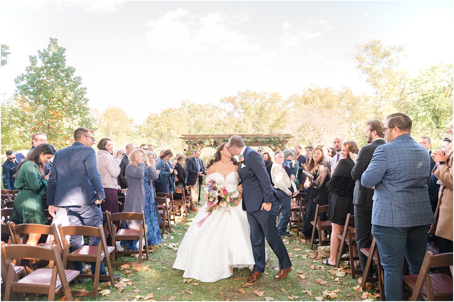 newlyweds kiss in the aisle after fall wedding ceremony outdoors on lawn at Bishop Hall Farmstead