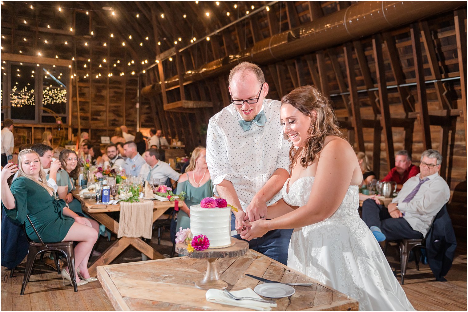 bride and groom cut wedding cake during wedding reception in barn