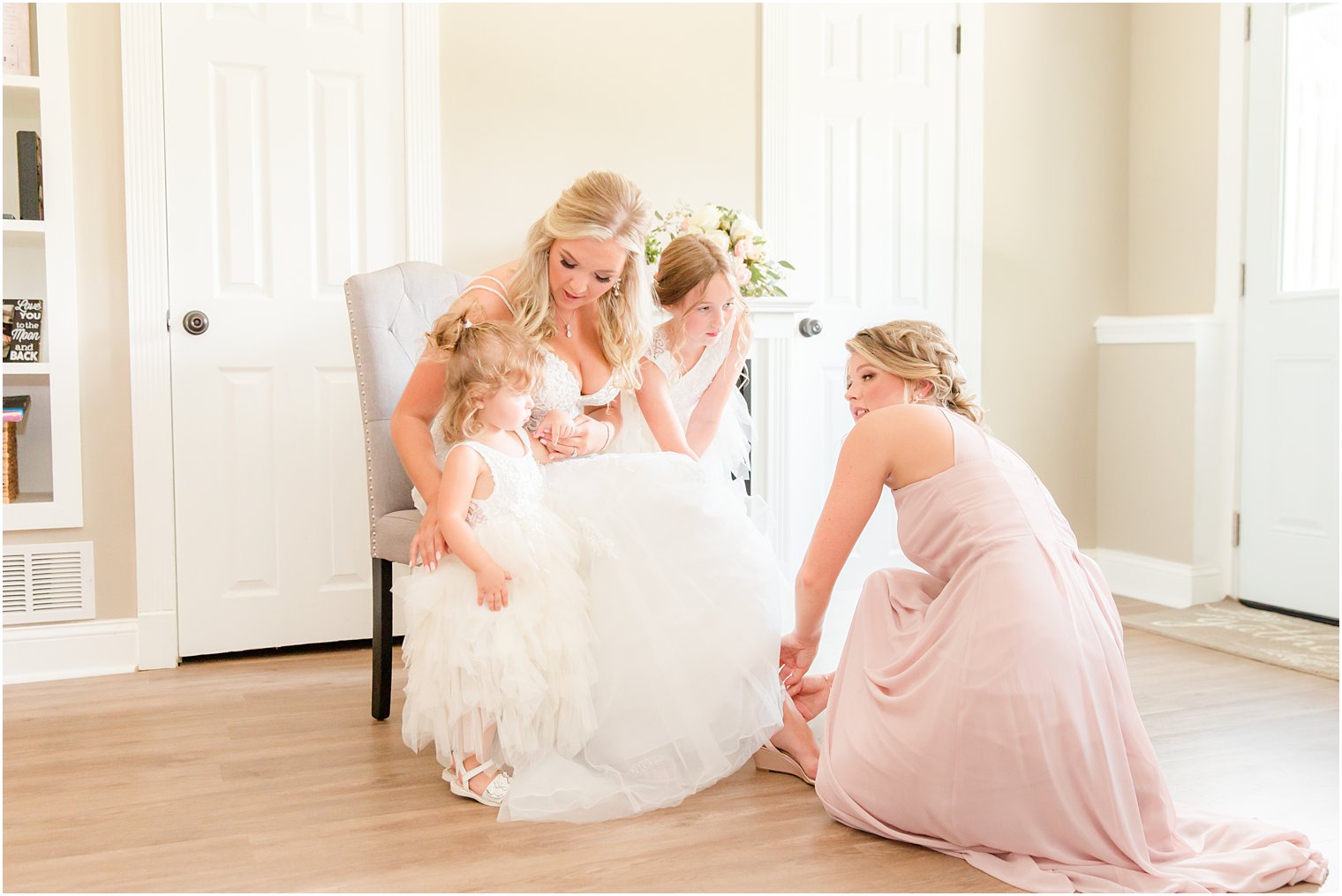bridesmaid in pink gown helps bride with shoes on wedding morning 