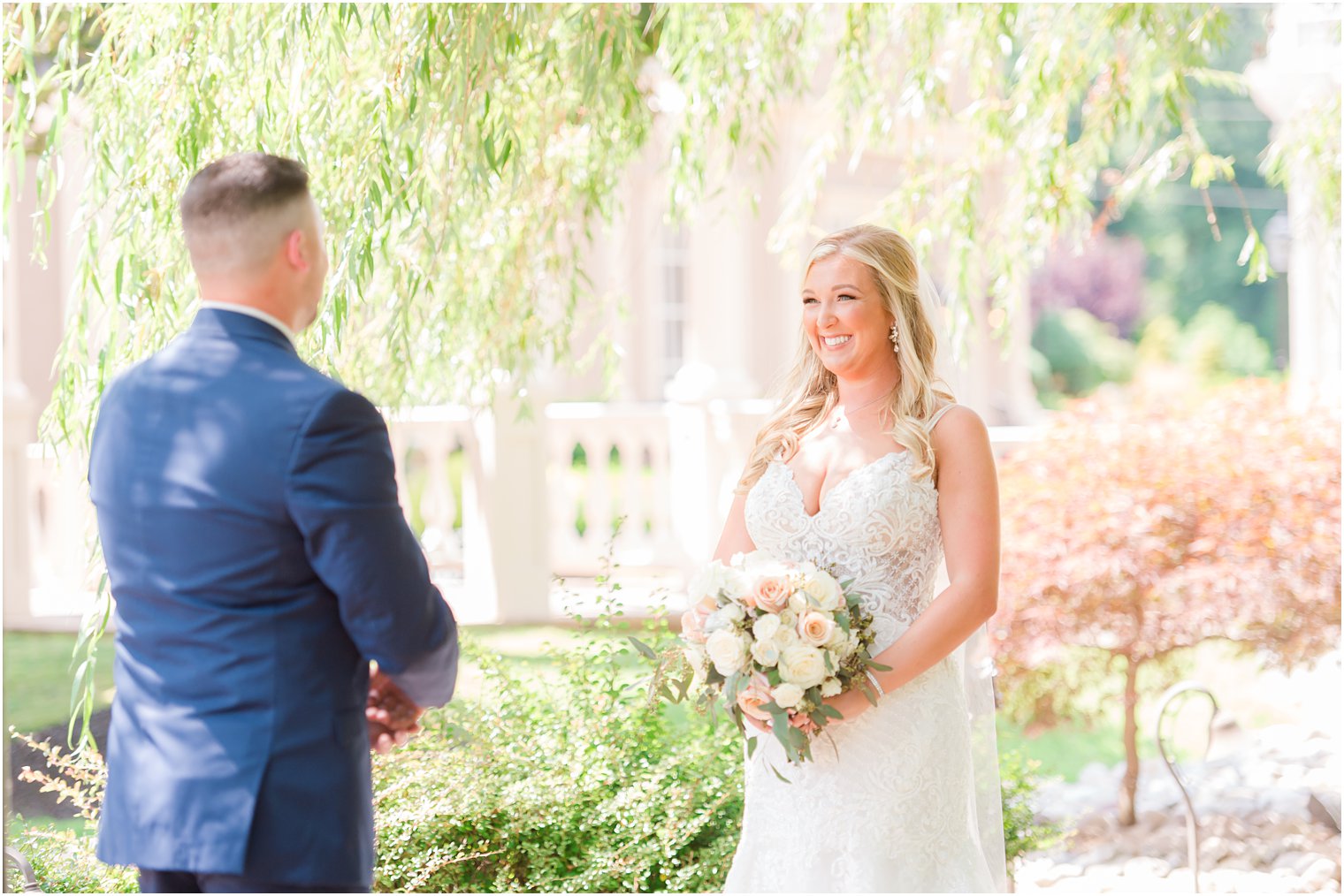 groom in navy suit turns to look at bride holding bouquet for first look 