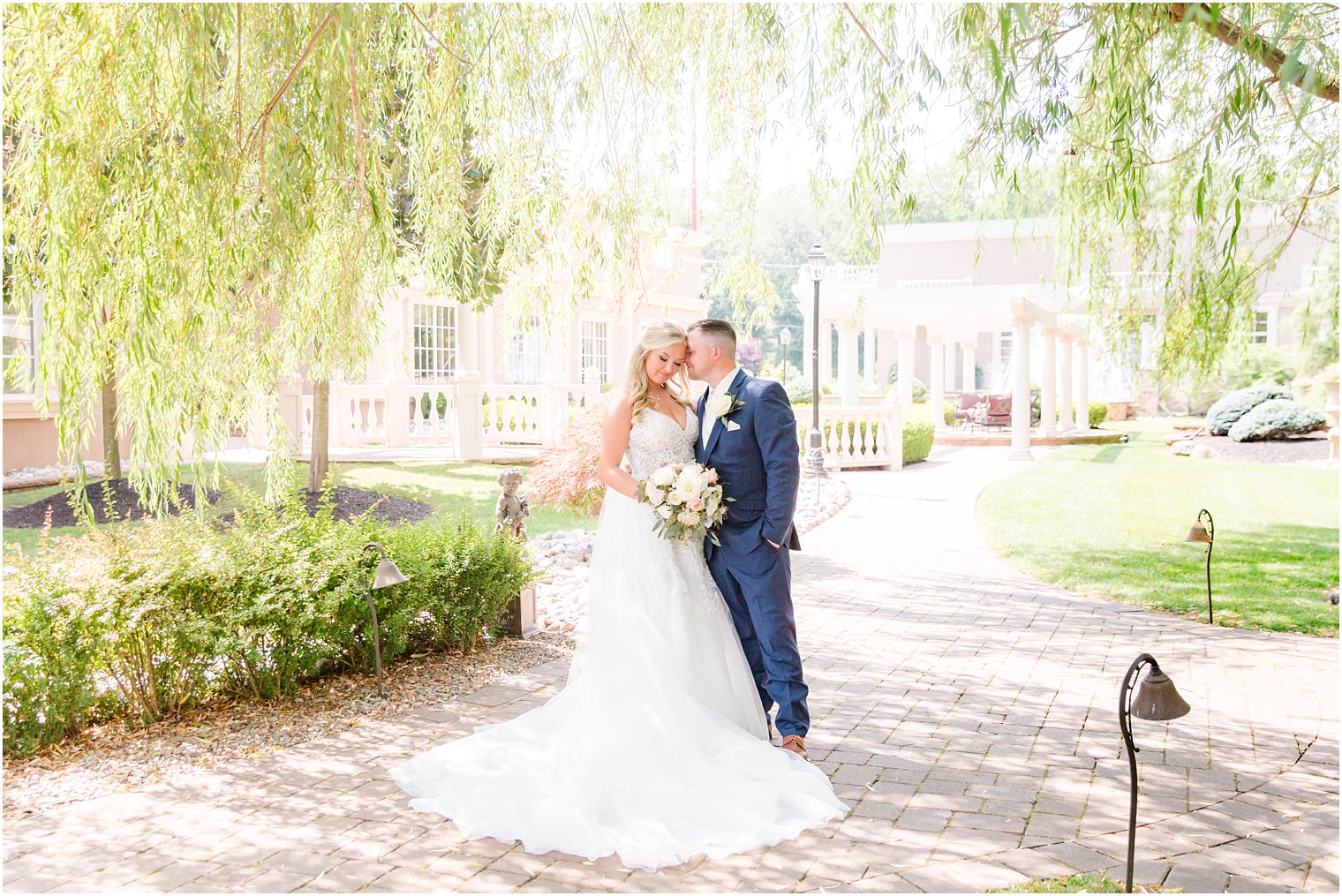 groom kisses the side of bride's head during portraits under willow tree