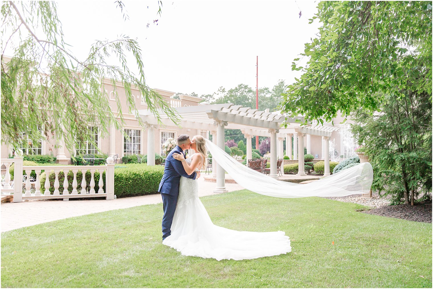 bride and groom kiss on lawn at Brigalia's with bride's veil floating behind them 