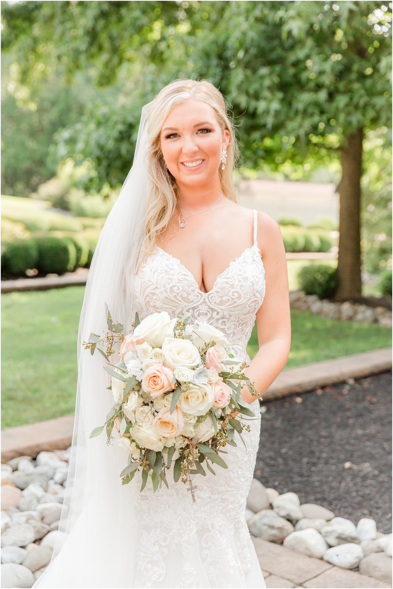 bride stands in v-neck wedding gown with pastel ivory and pink bouquet of roses 