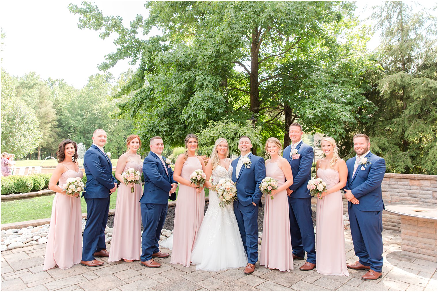 bride and groom pose with wedding party in pastel pink gowns and navy suits 