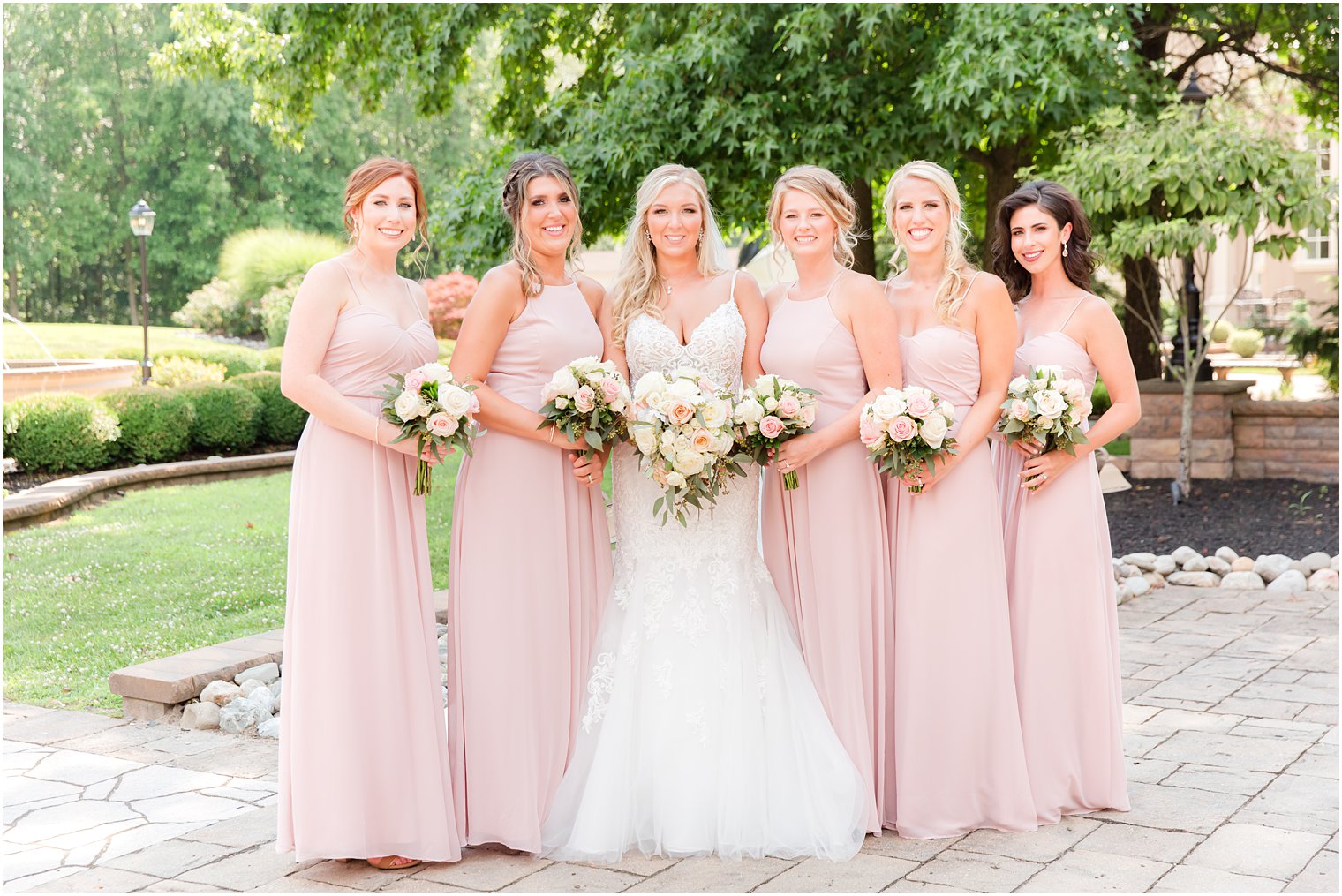 bride poses with bridesmaids in pink gowns with white rose bouquets