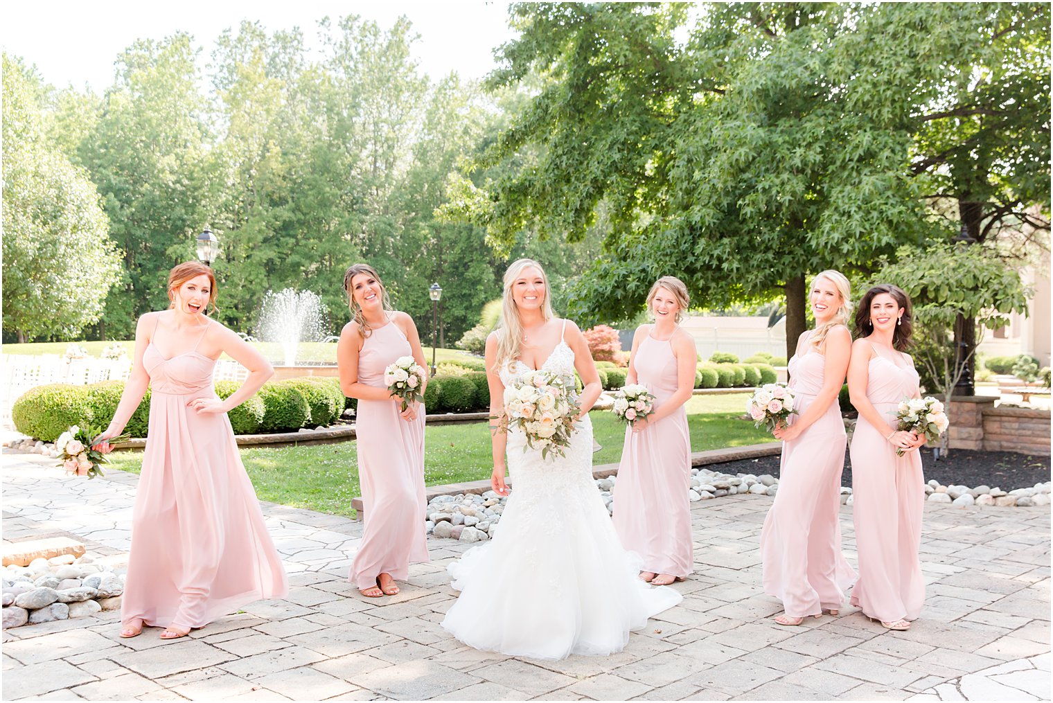 bride poses with bridesmaids in pastel pink gowns on patio at Brigalia's