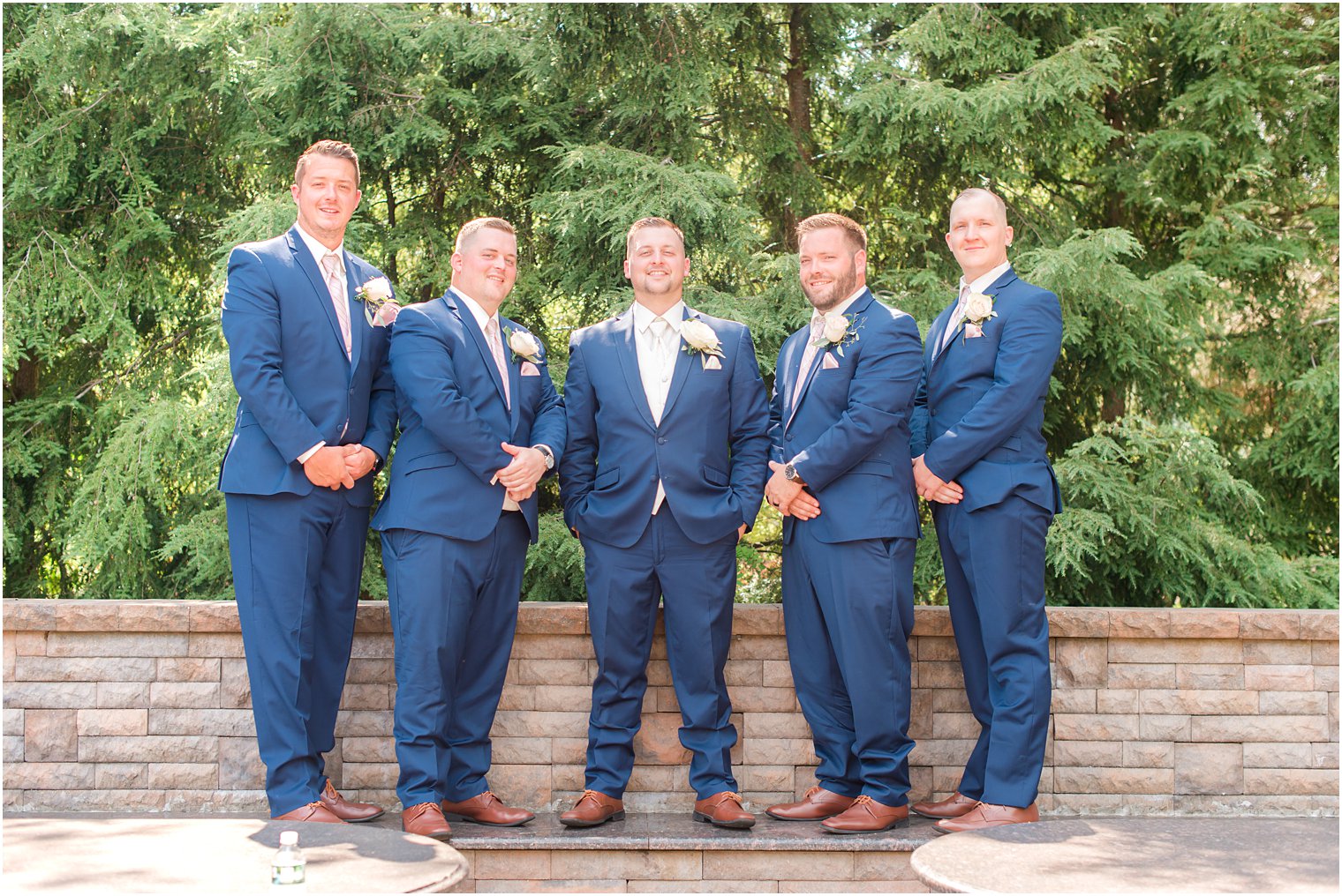 groom stands with groomsmen in navy suits by brick wall at Brigalia's