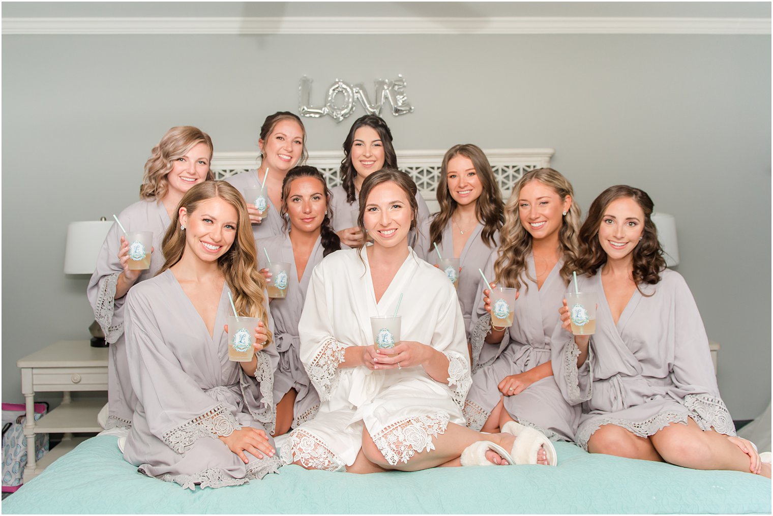 bride sits on bed with bridesmaids in matching gowns with custom cups at Crystal Point Yacht Club
