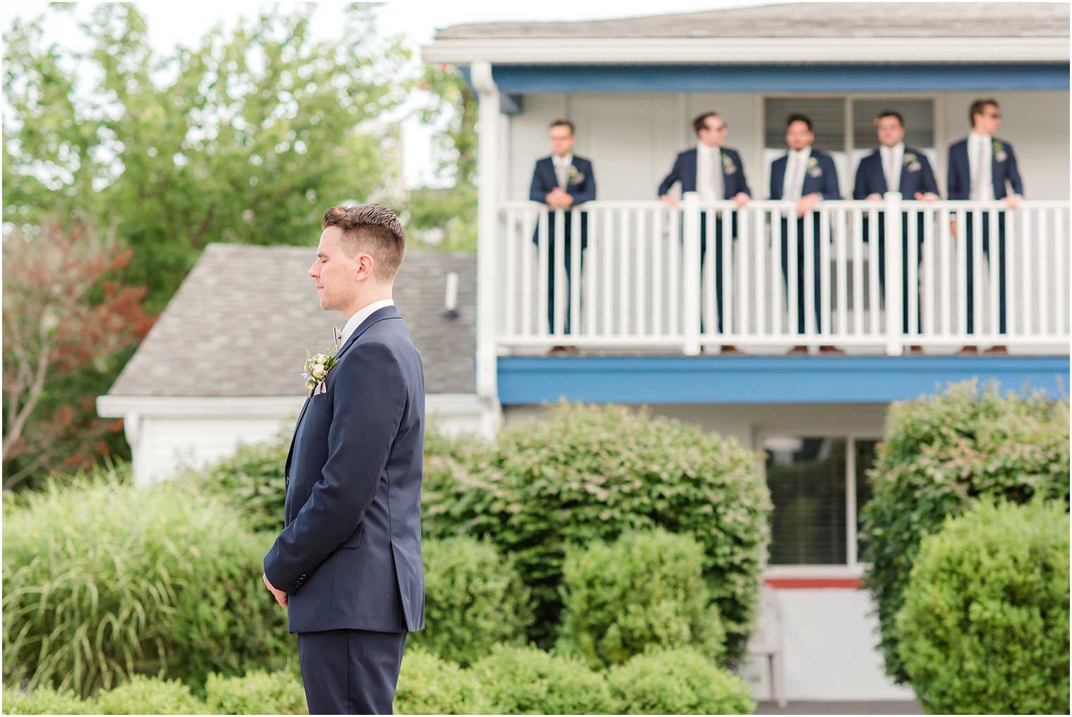 groom waits for first look with bride while groomsmen watch from balcony 