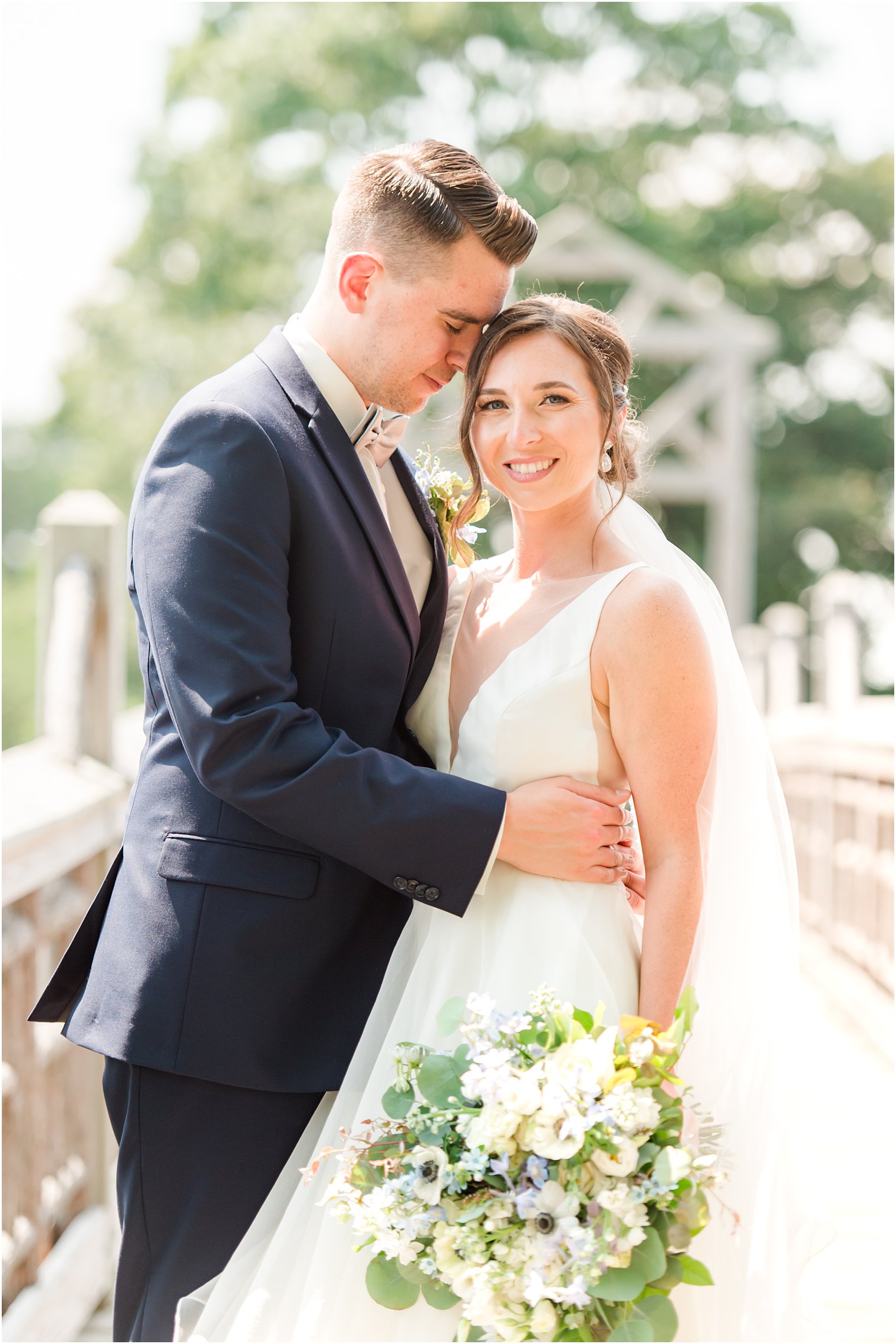 groom leans head down to hug bride to his hip on bridge at Spring Lake Park