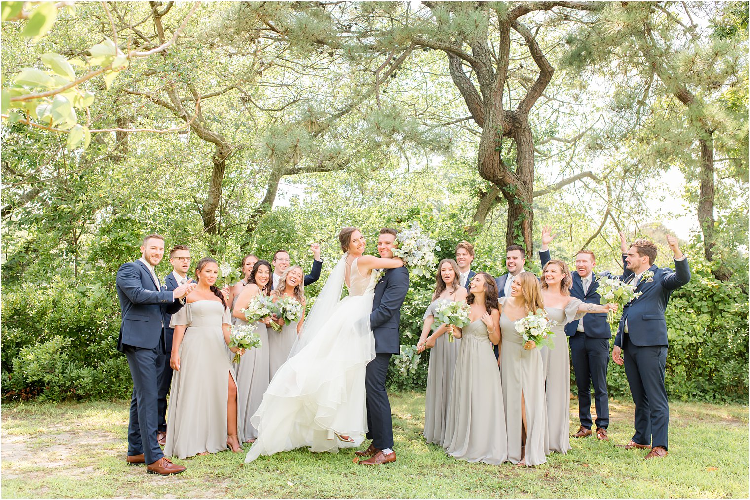 groom lifts bride hugging her in front of wedding party