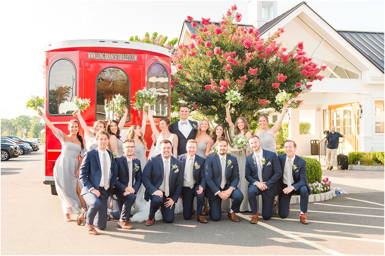 newlyweds cheer with wedding party kneeling by red trolley at Crystal Point Yacht Club