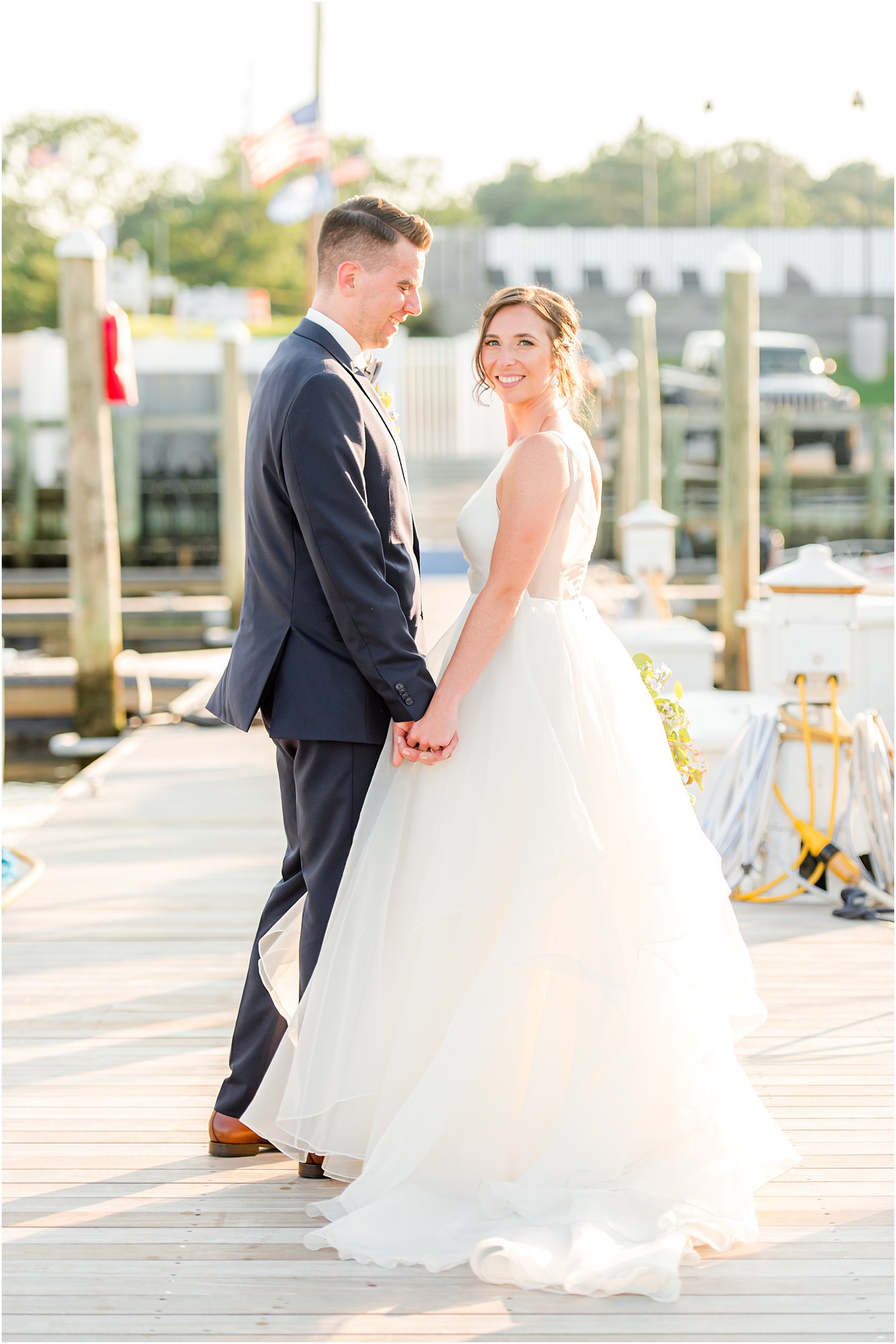bride and groom hold hands looking back over shoulders on dock at Crystal Point Yacht Club