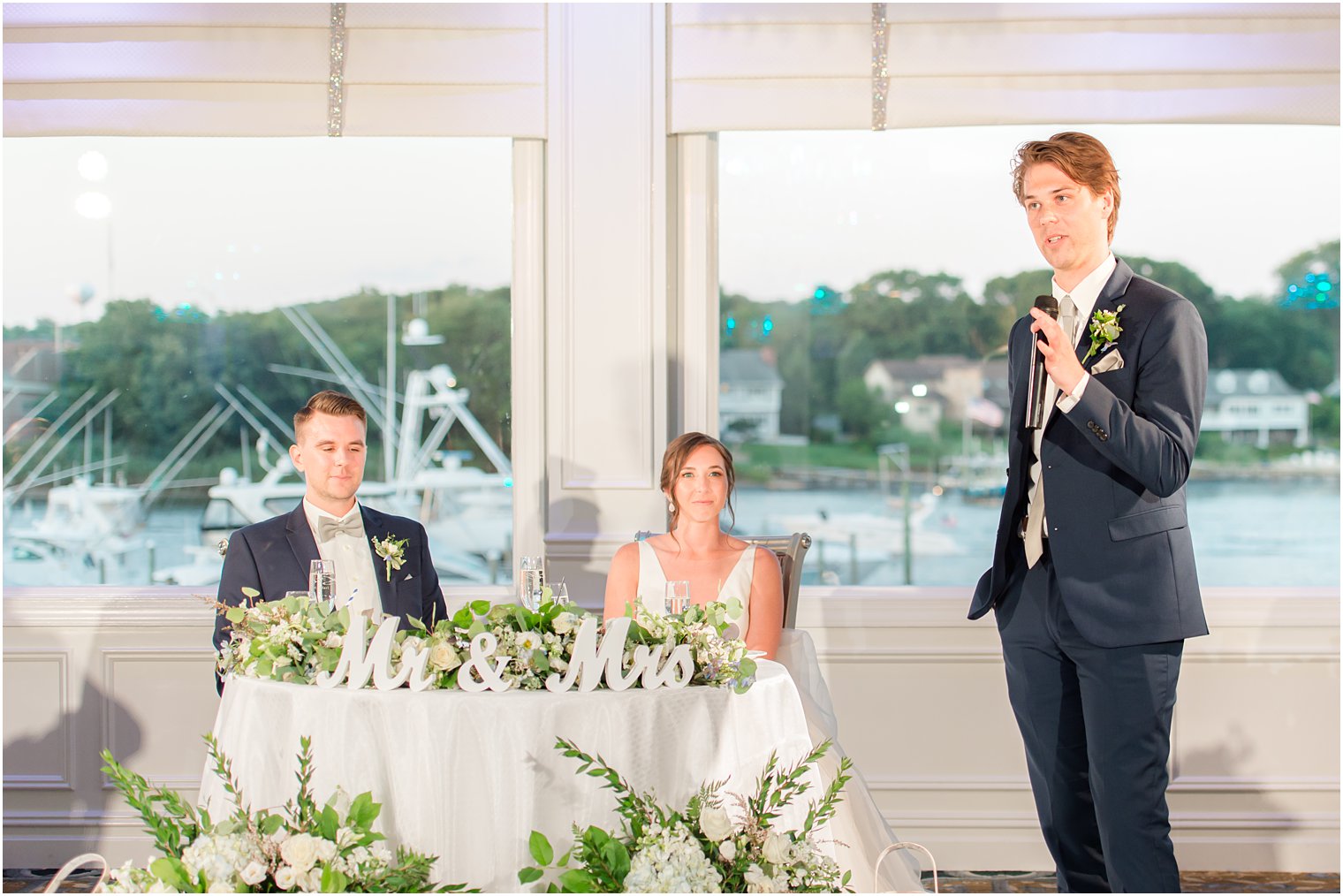 groomsman gives speech by sweetheart table with bride and groom 