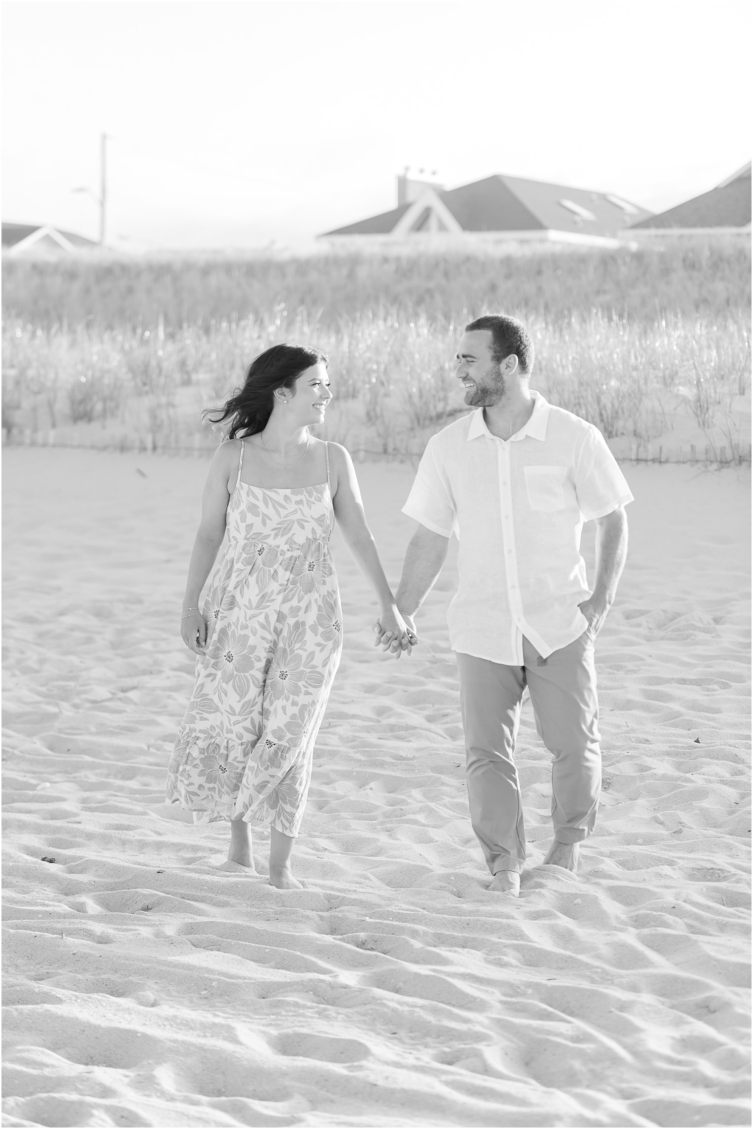 engaged couple holds hands walking through sand at Lavallette Beach