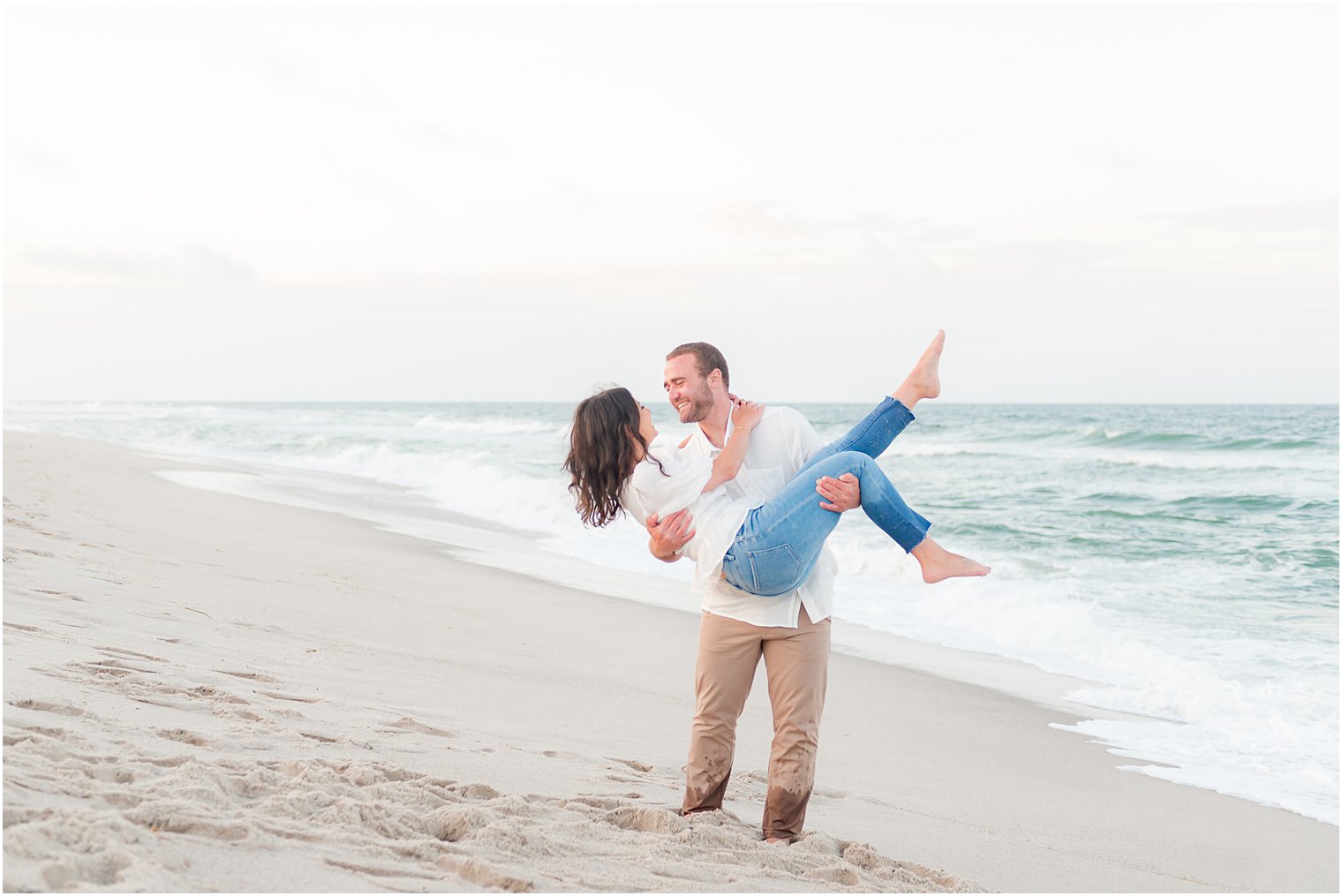 groom lifts up bride while she kicks her feet during casual summer engagement session at Lavallette Beach