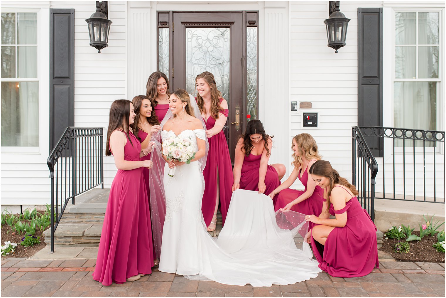 bridesmaids in magenta gowns help bride with veil and dress