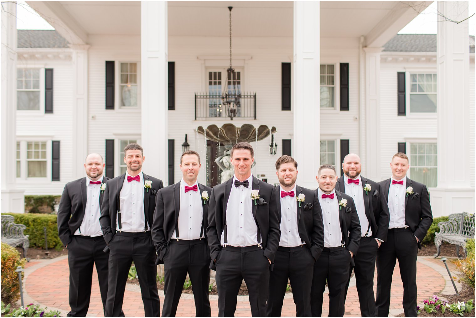 groom stands with groomsmen with hands in pockets showing off colored ties