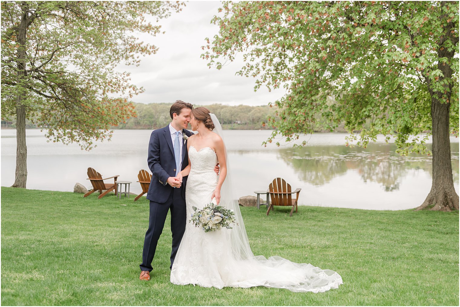 bride and groom lean heads together in front of lake