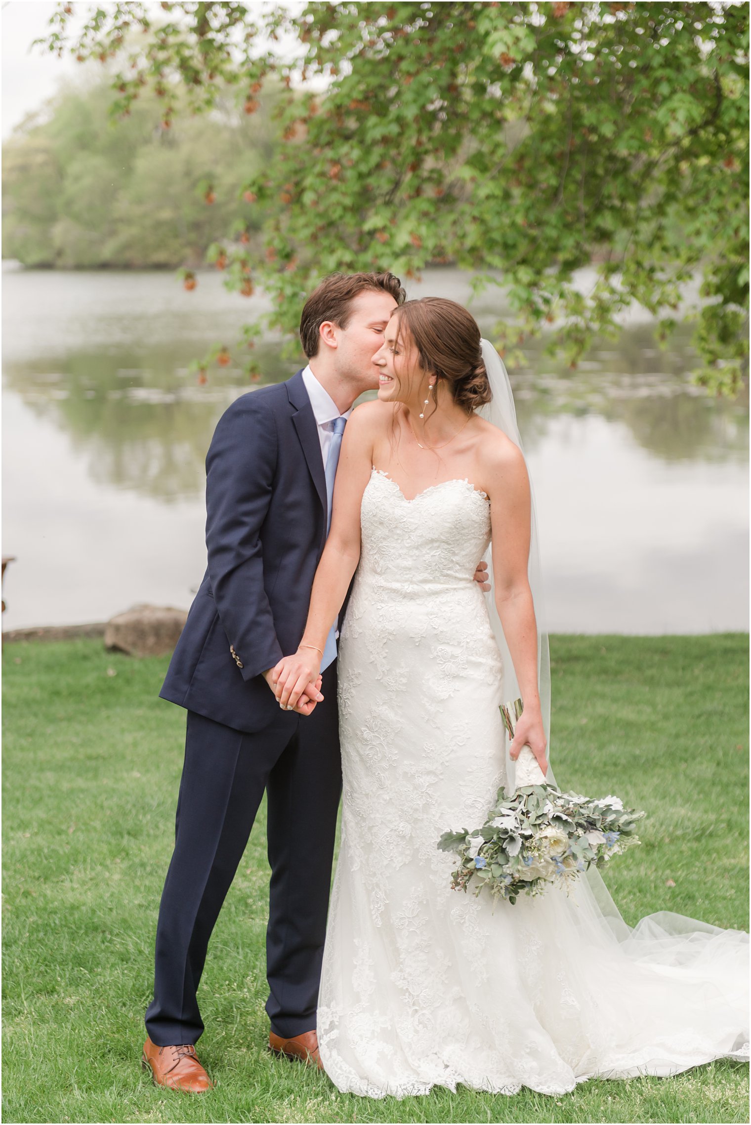 groom leads to kiss bride's cheek in front of lake at Indian Trail Club