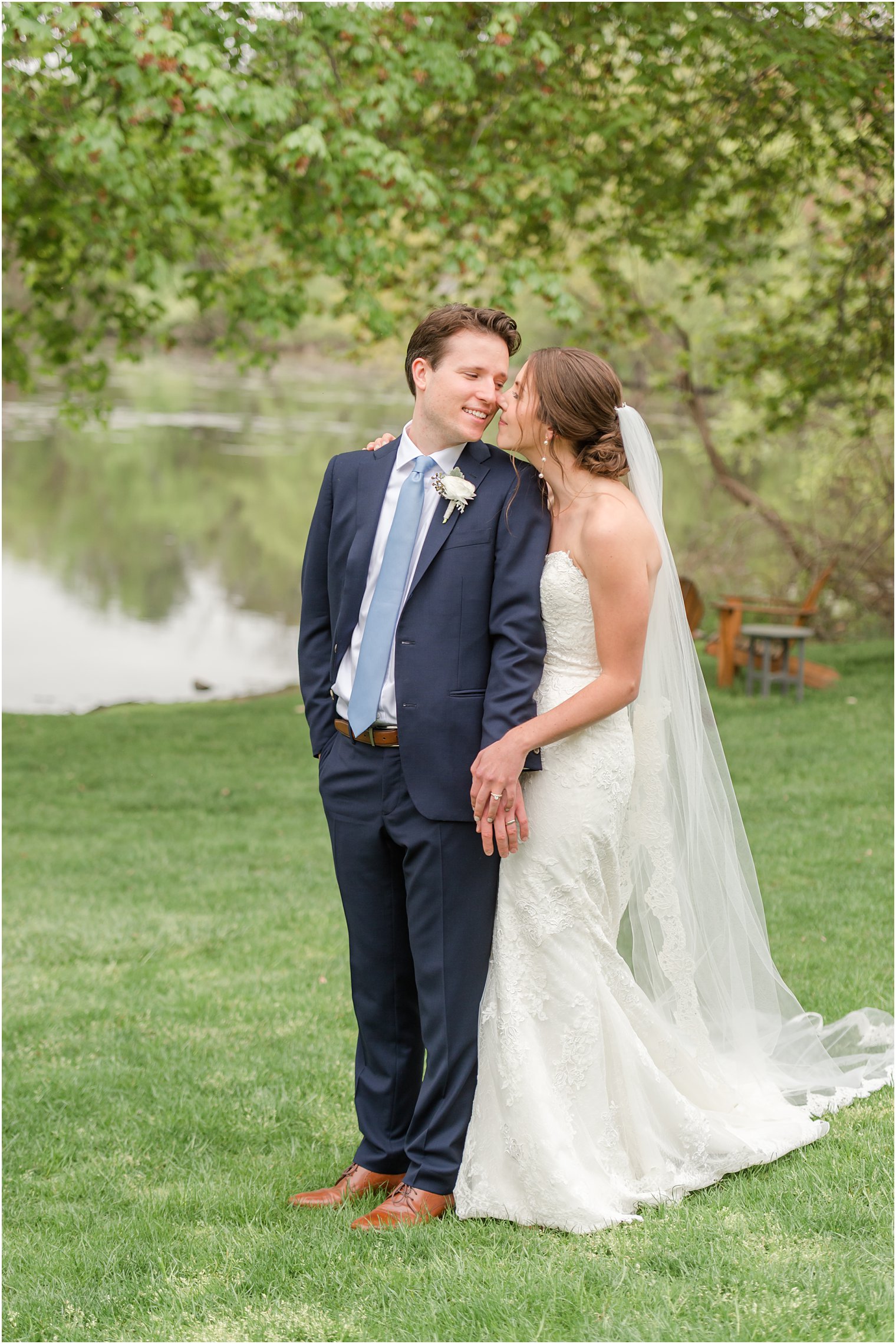 bride stands behind groom leaning to kiss his cheek
