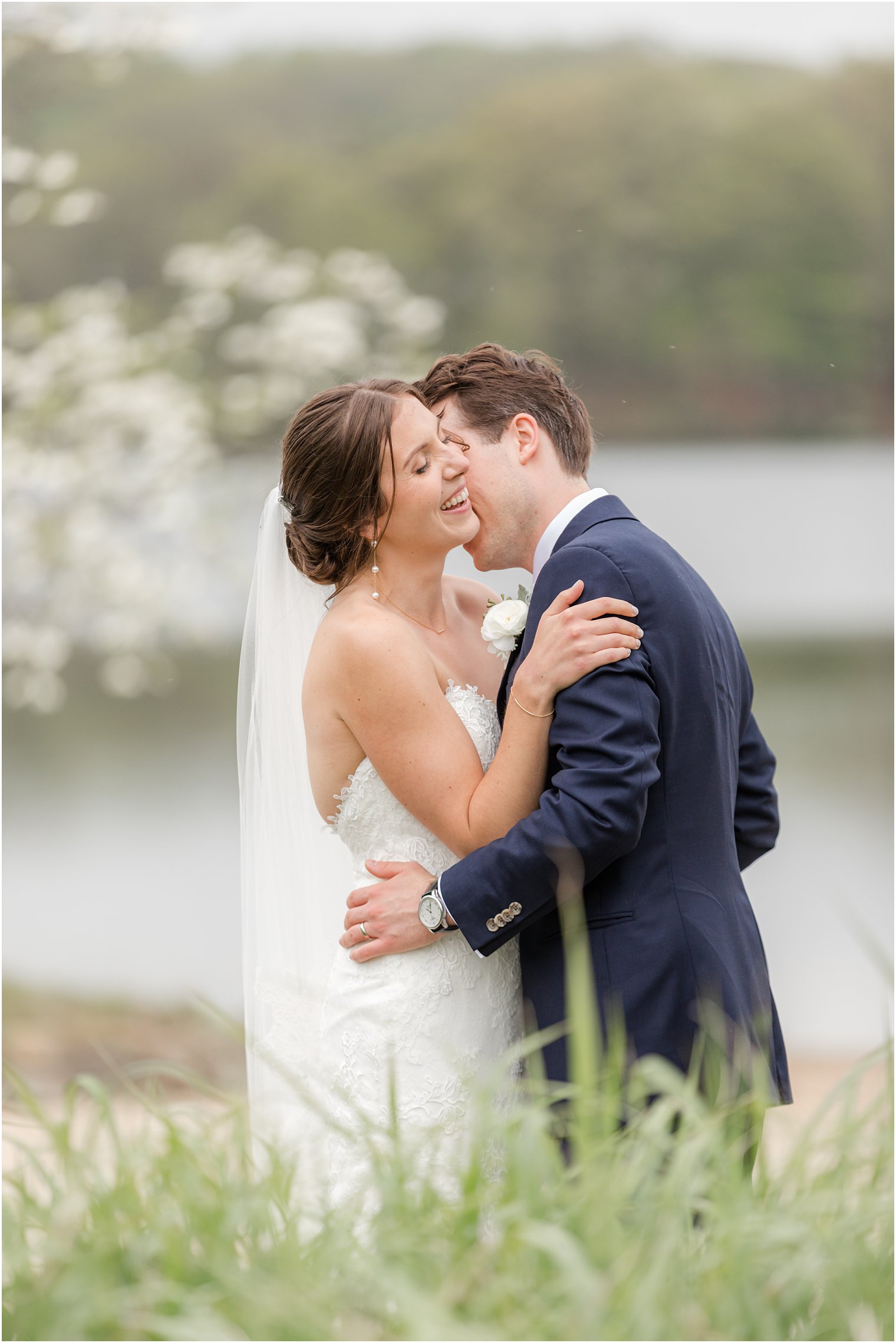 husband leans to kiss wife's neck during portraits bywaterfront at Indian Trail Club