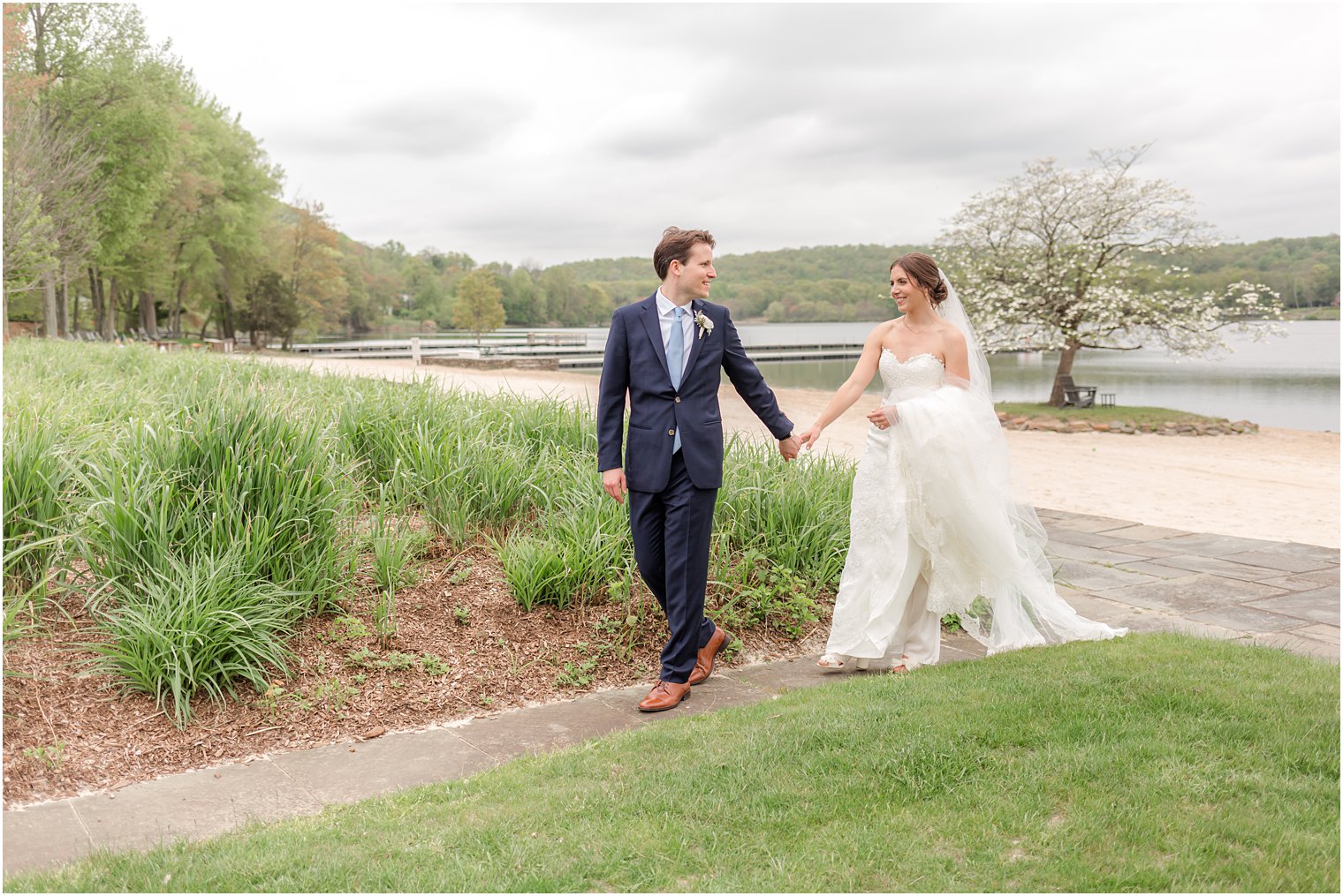 newlyweds hold hands walking on pathway by lake at Indian Trail Club