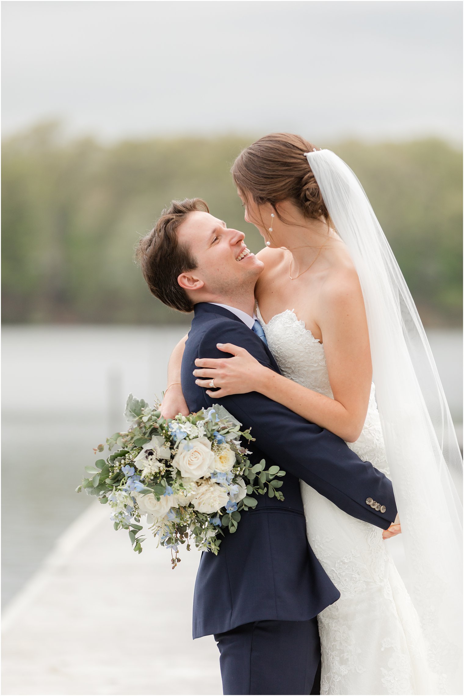 groom smiles up at bride lifting her on dock 