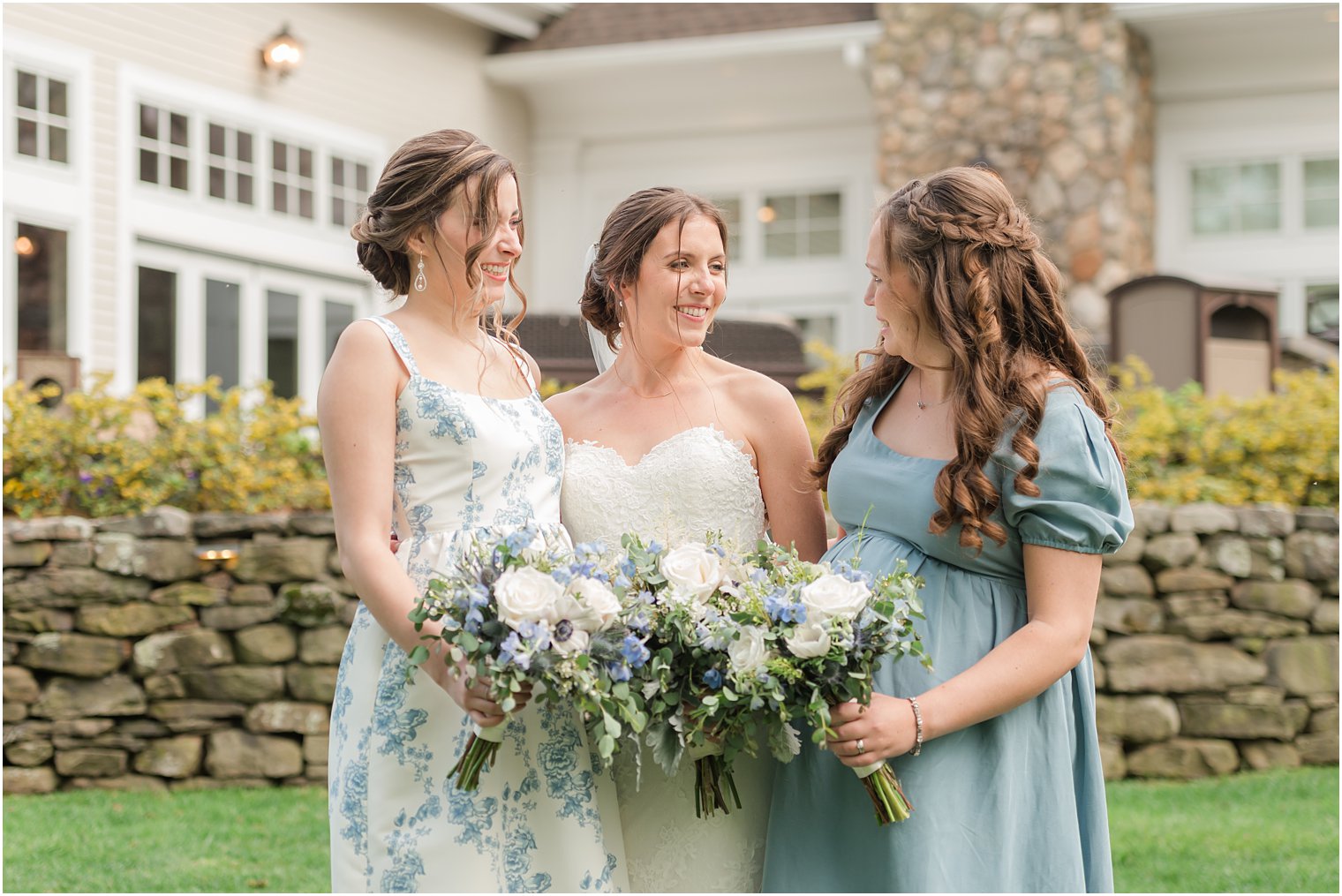 bridesmaids smile with bride standing by stone wall at Indian Trail Club