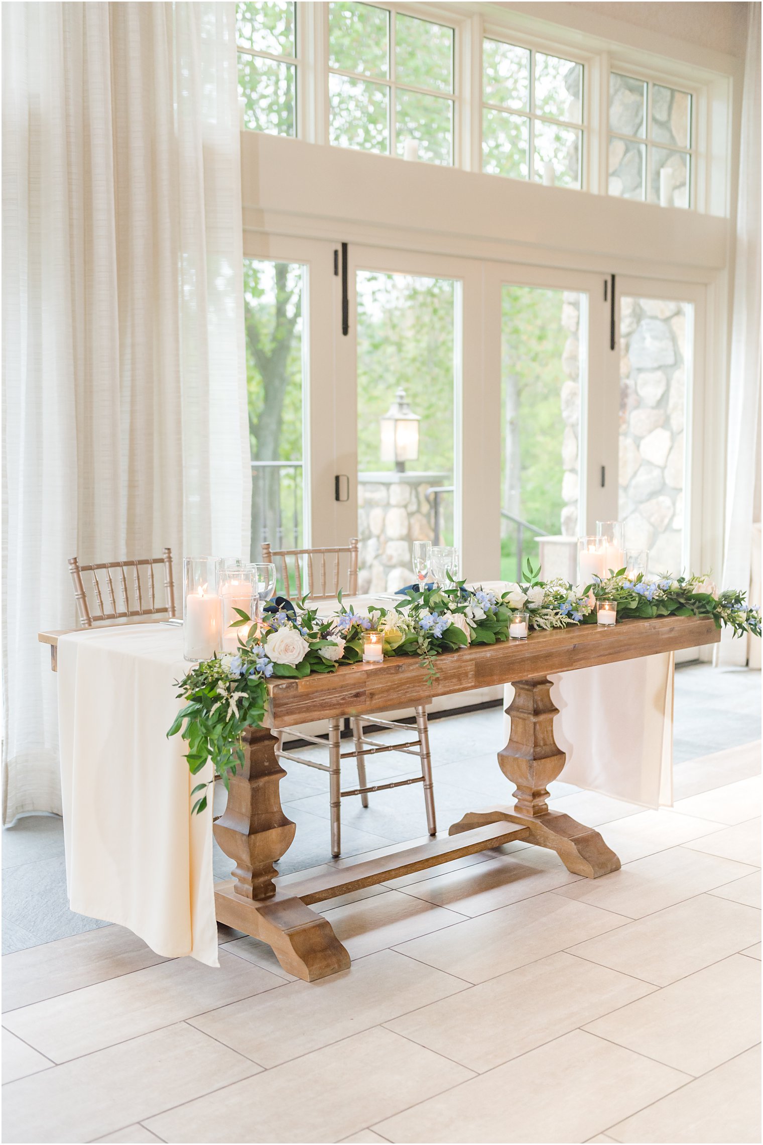 sweetheart table with white and blue flowers draped on greenery 
