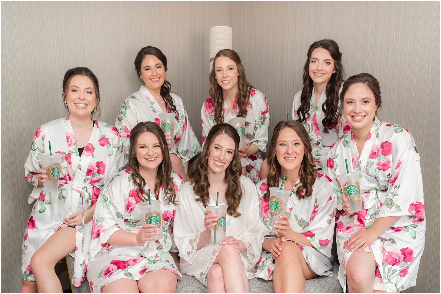 bride sits with bridesmaids in floral robes with Starbucks cups 