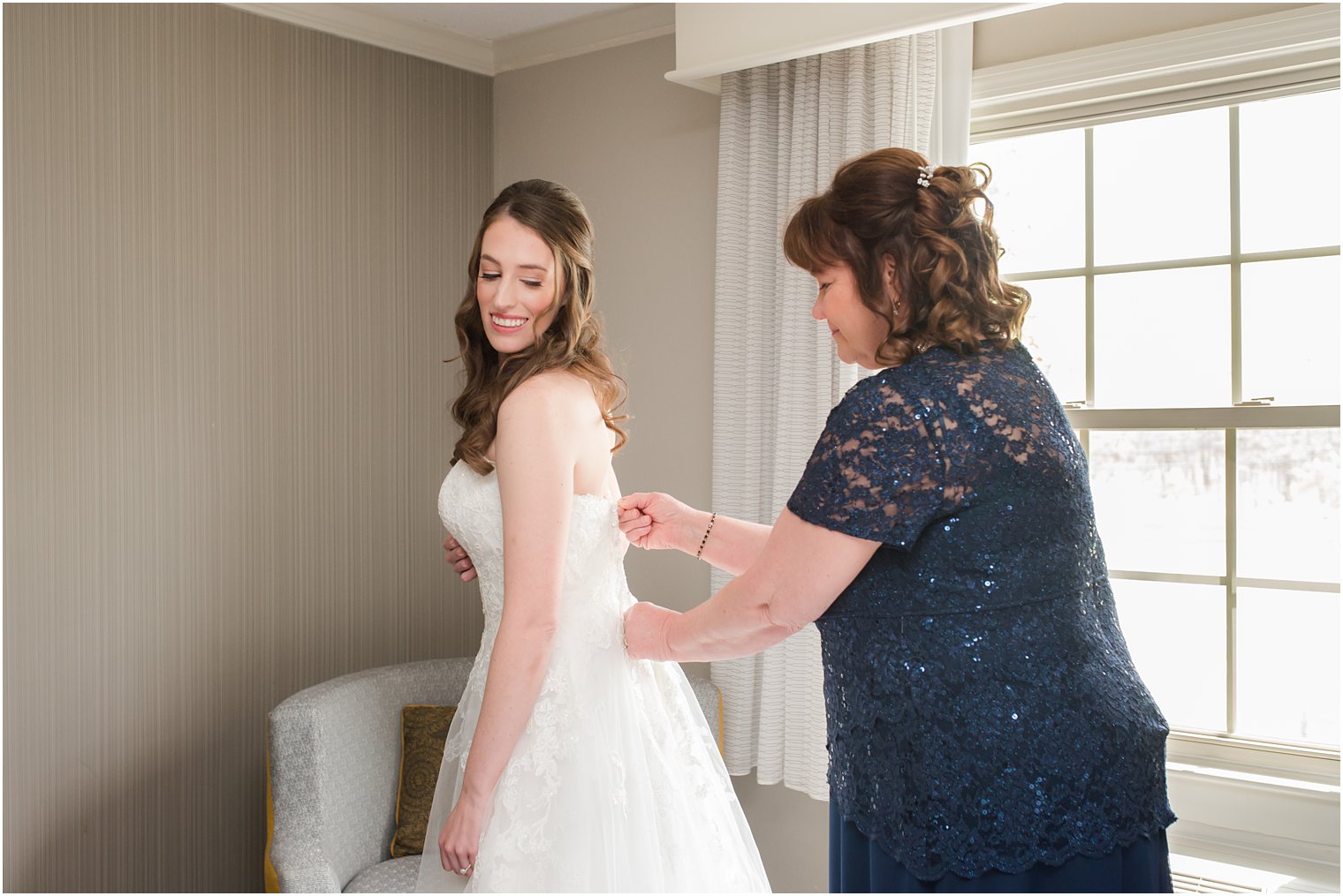 mother zips up bride in wedding gown at English Manor
