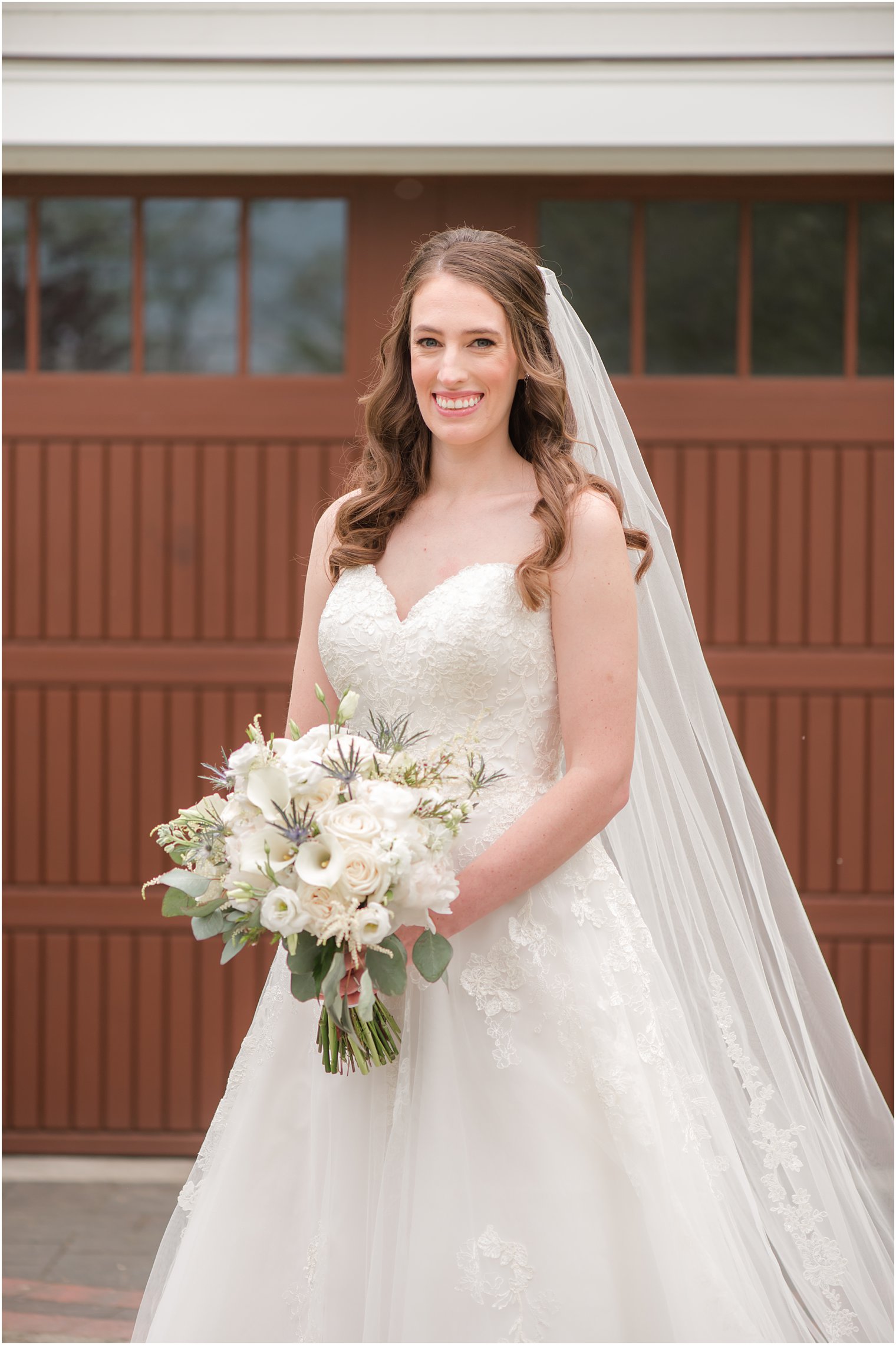 bride stands outside wooden door holding white bouquet 