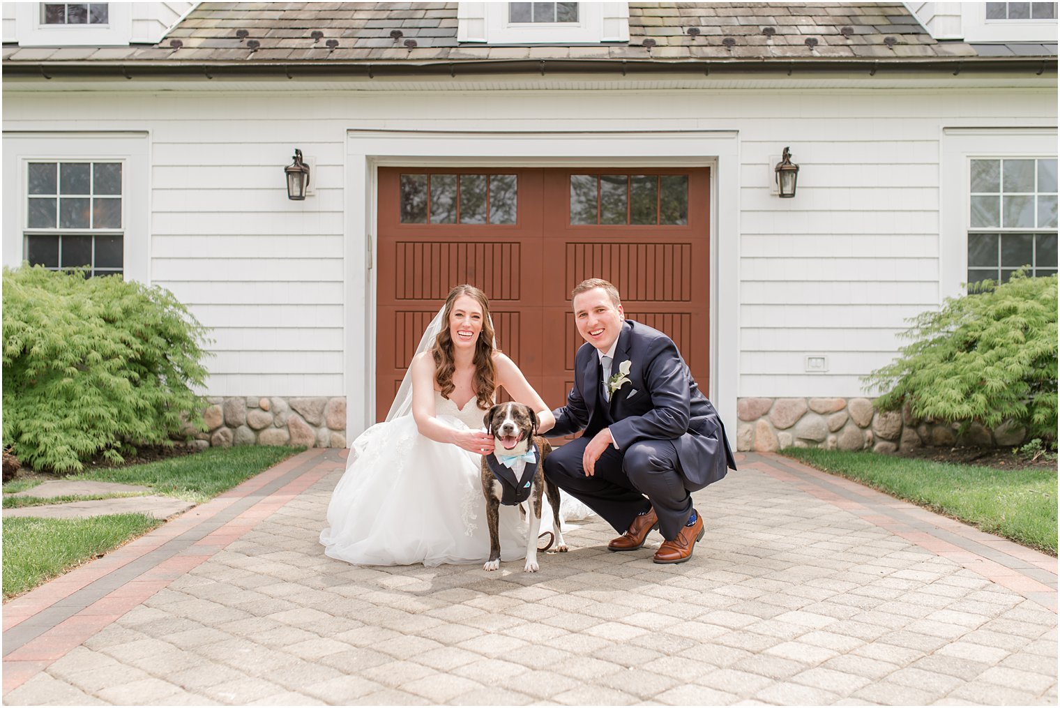 bride and groom kneel by wood doors at The English Manor with dog 