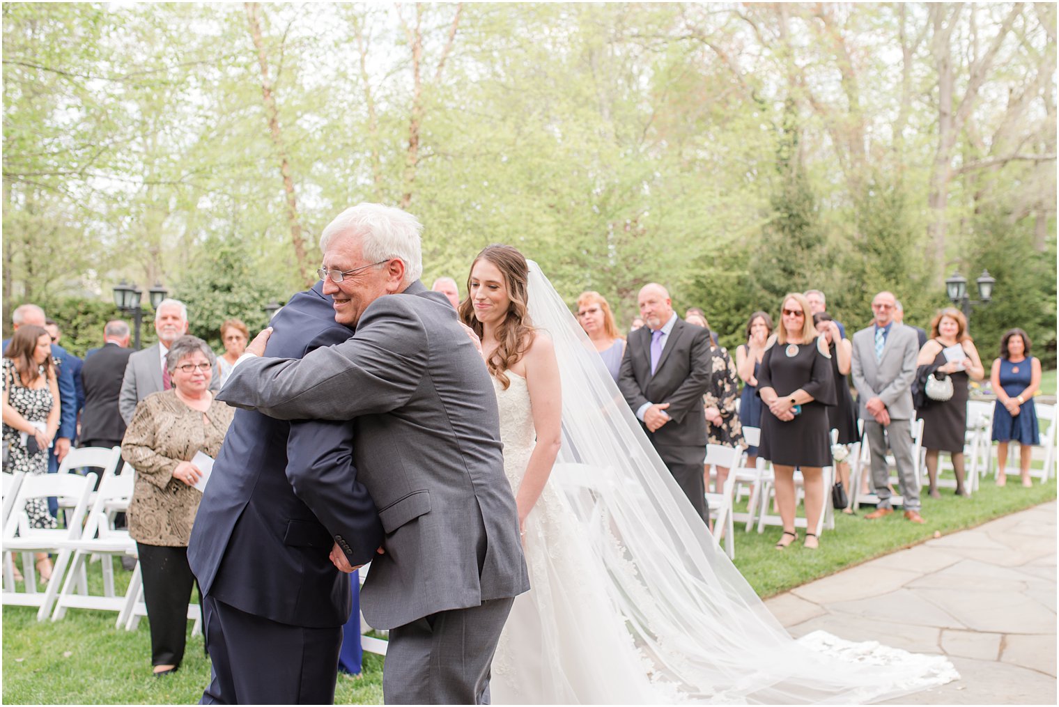 father hugs groom during garden wedding ceremony 